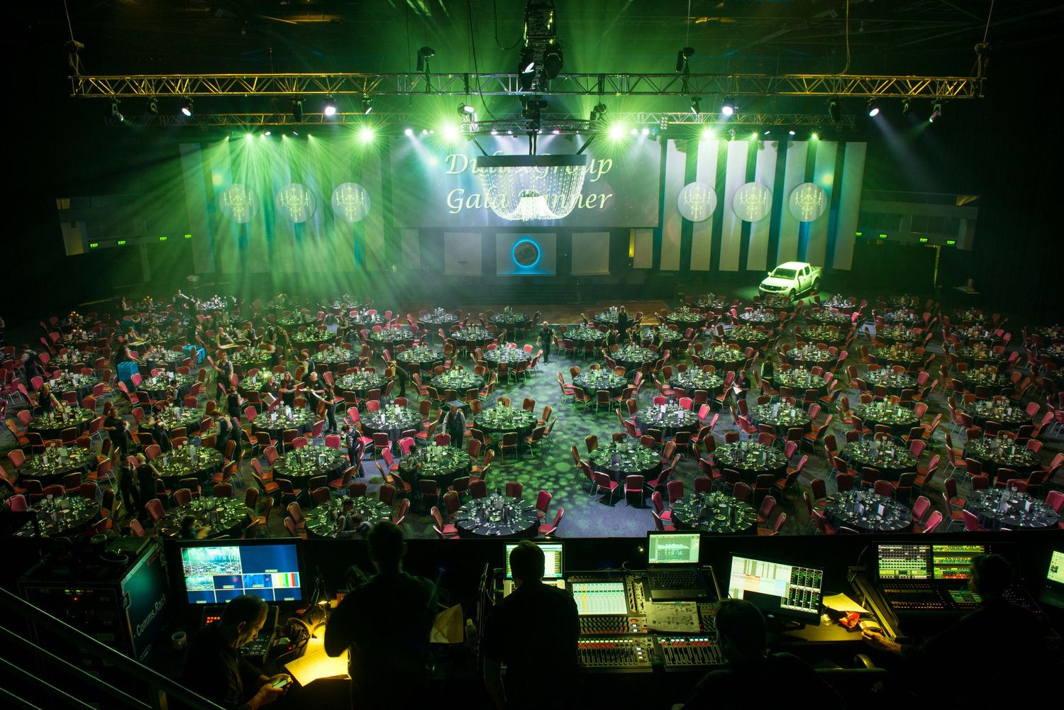 Aerial view of a large gala dinner event with round tables, green lighting, and a stage in a grand venue.