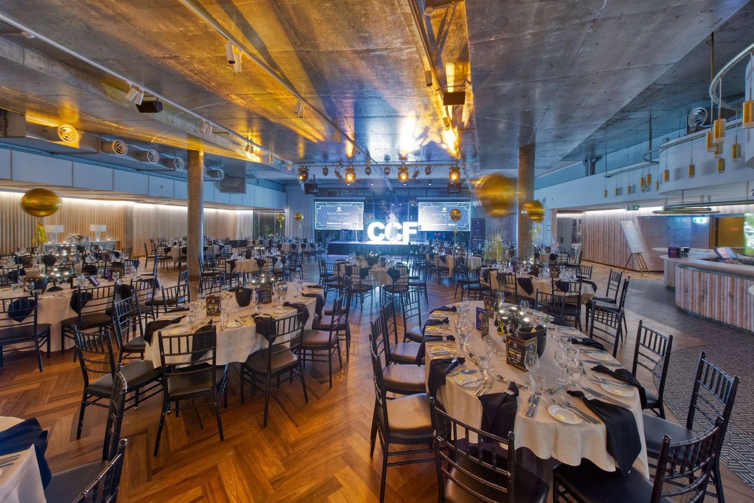 Elegant banquet hall with round tables set for formal dinner under warm industrial ceiling lights.