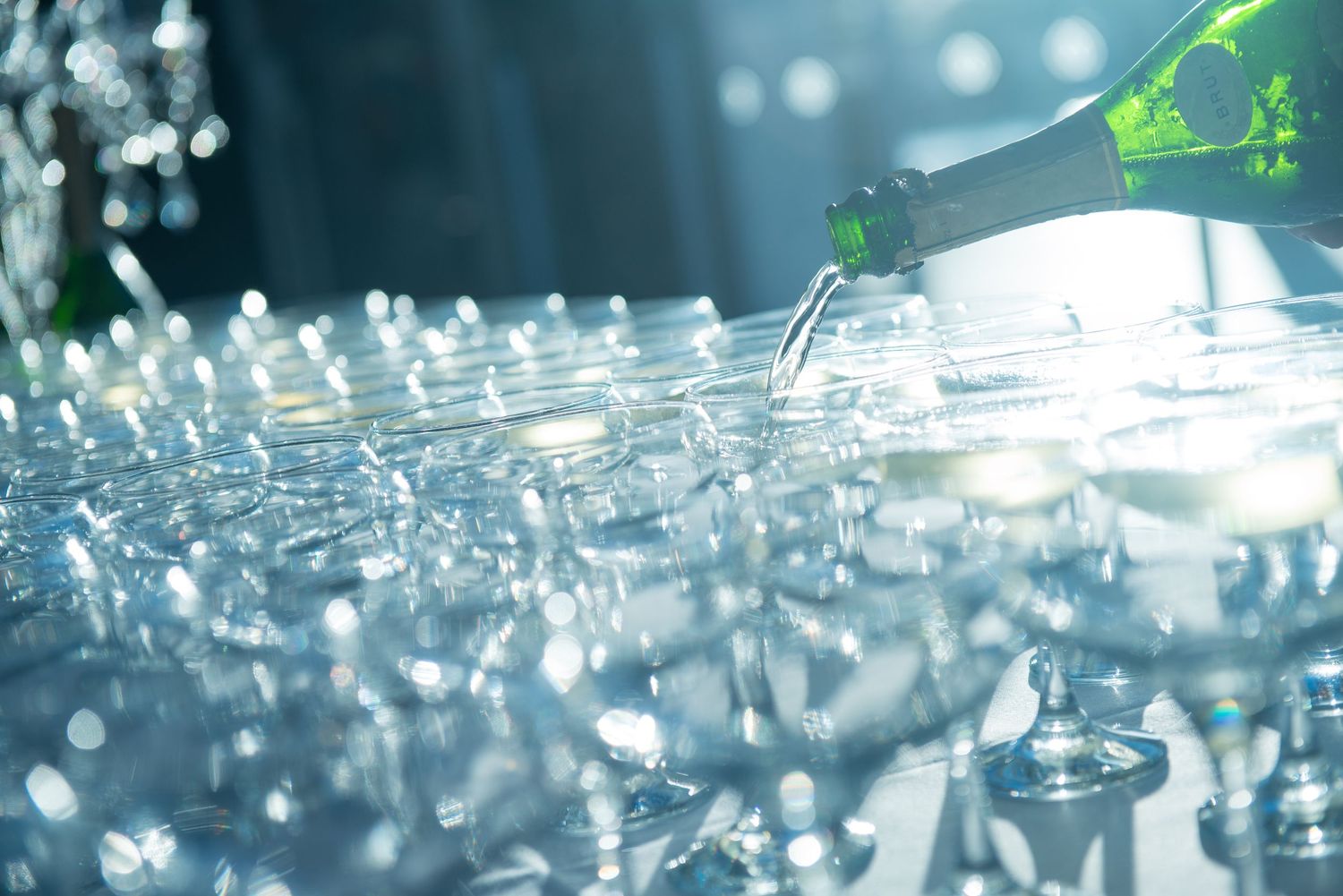 Champagne being poured into rows of sparkling crystal glasses at a formal event.