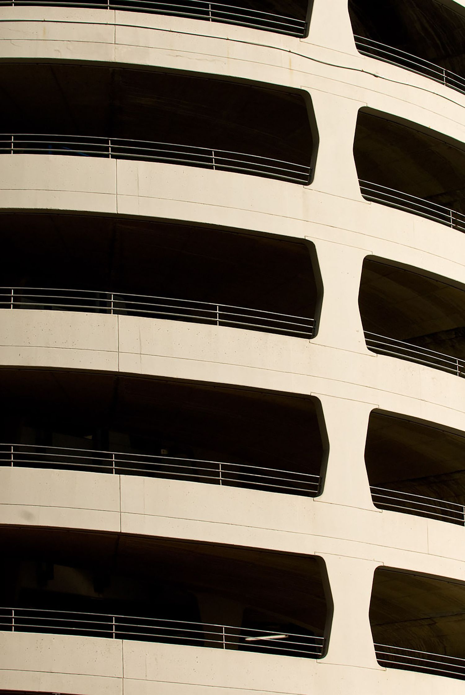 Curved multi-story parking garage exterior with horizontal balconies in black and white architectural photography.