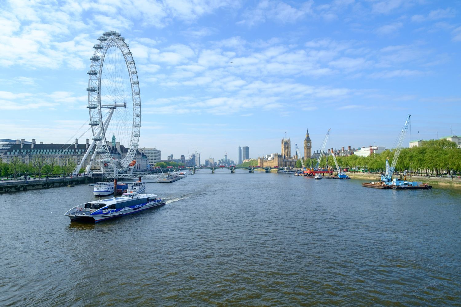 London Eye ferris wheel and Big Ben along the River Thames on a sunny day.