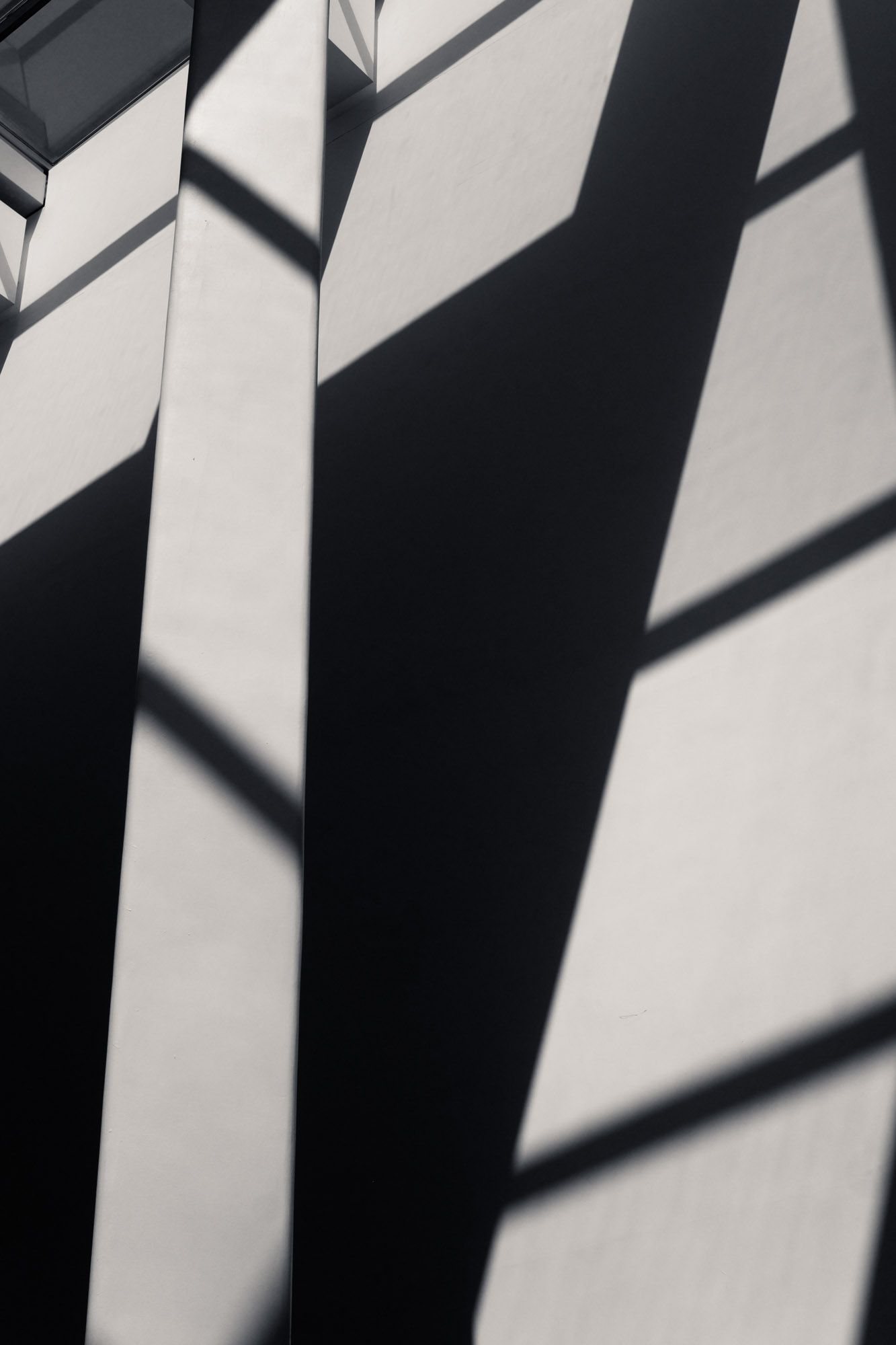 Abstract black and white architectural photo of sharp diagonal shadows cast on a concrete wall.