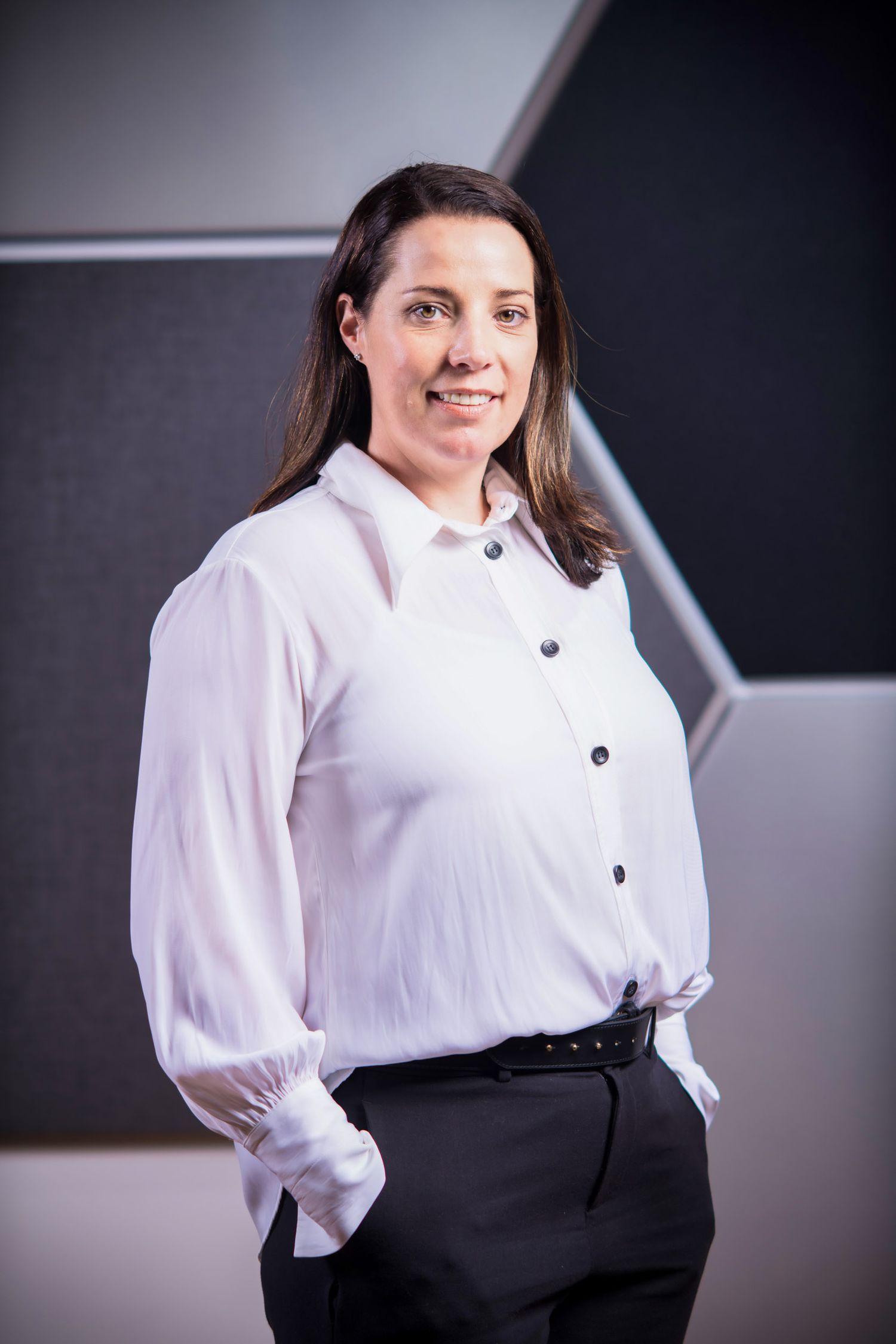 Professional portrait of a smiling woman in a white blouse and black pants standing confidently.