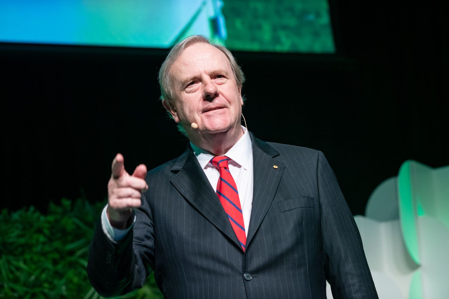 Man in pinstripe suit pointing at camera on stage.