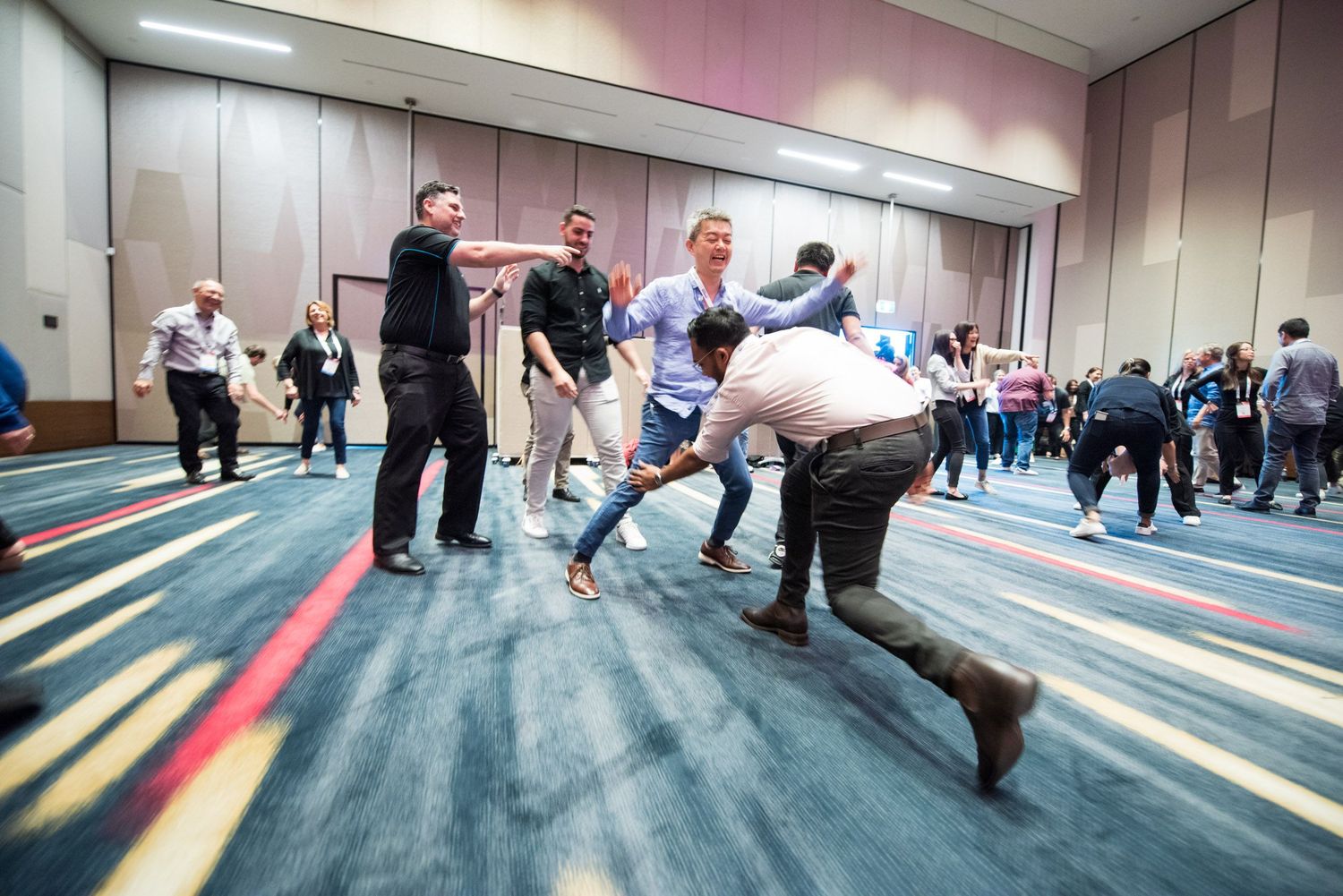 Conference attendees participate in an interactive group activity on a colorful carpeted ballroom floor.