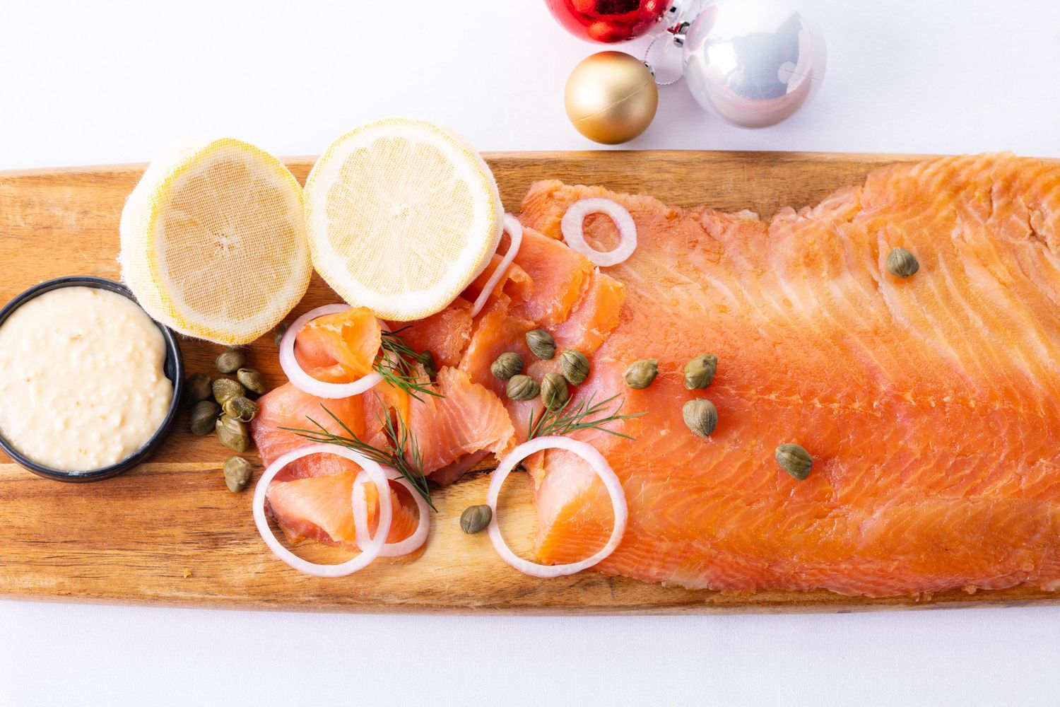 Smoked salmon platter with capers, onion rings, lemon halves, and creamy sauce on a wooden board.