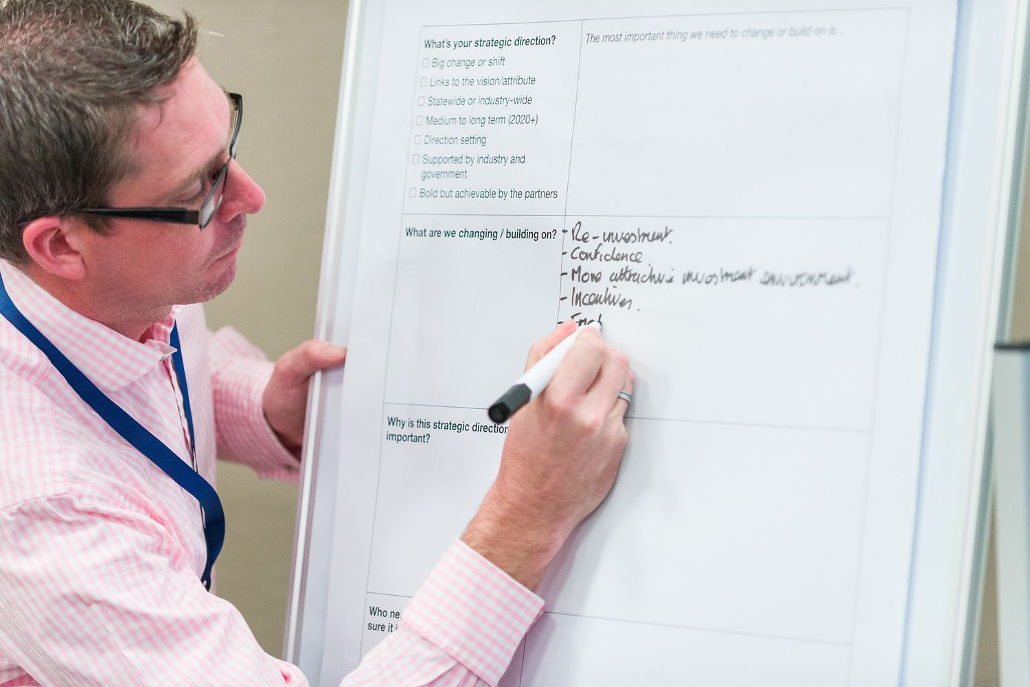 Business professional writing notes on a whiteboard during a corporate workshop or training session.
