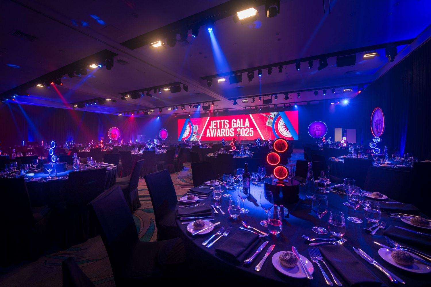 Grand ballroom set for the Jets Gala Awards with dramatic blue and red lighting and round dining tables.