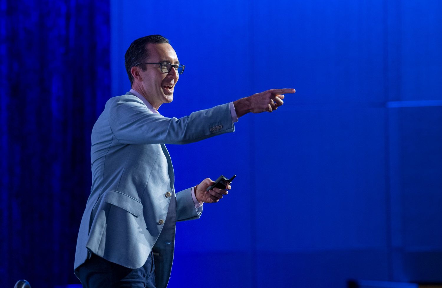 Smiling male speaker in blue blazer pointing on stage at corporate conference.