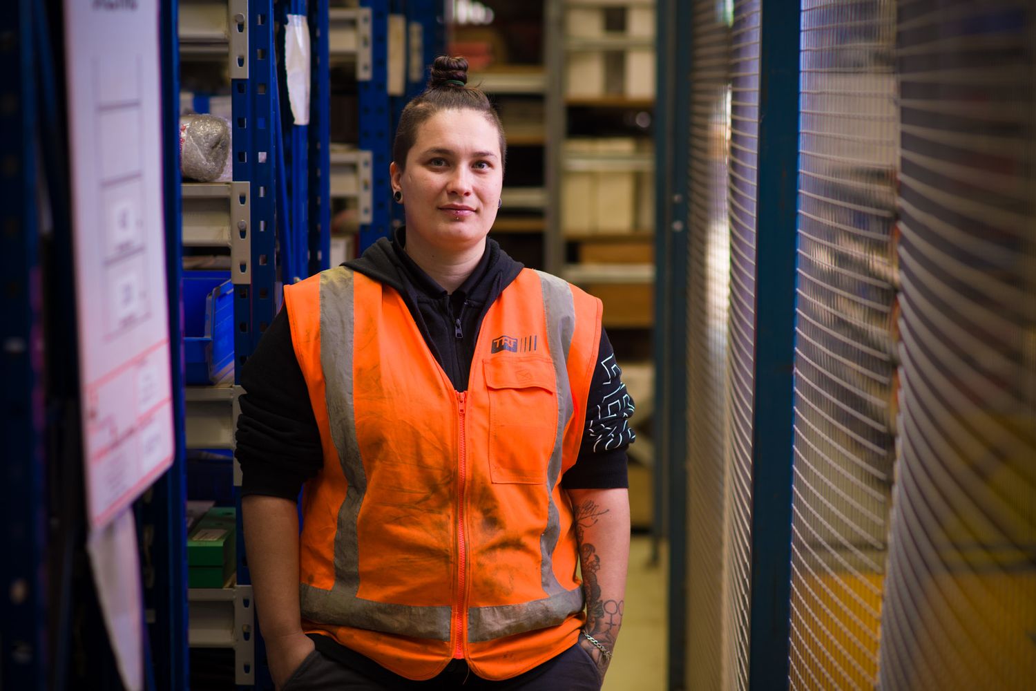 Young female warehouse worker in orange safety vest standing in a storage facility.