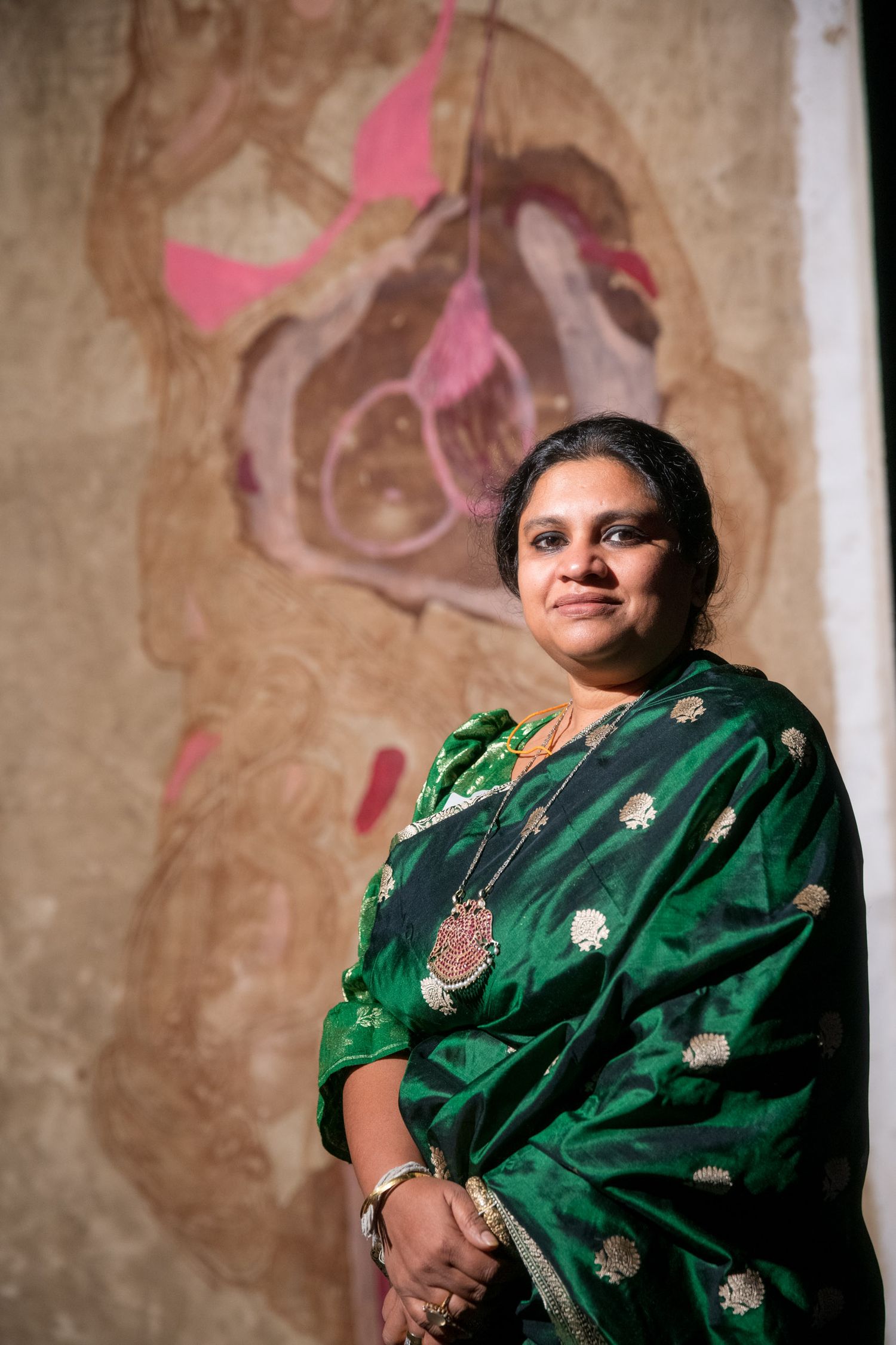 Woman in elegant green embroidered saree with silver jewelry standing before abstract artwork.
