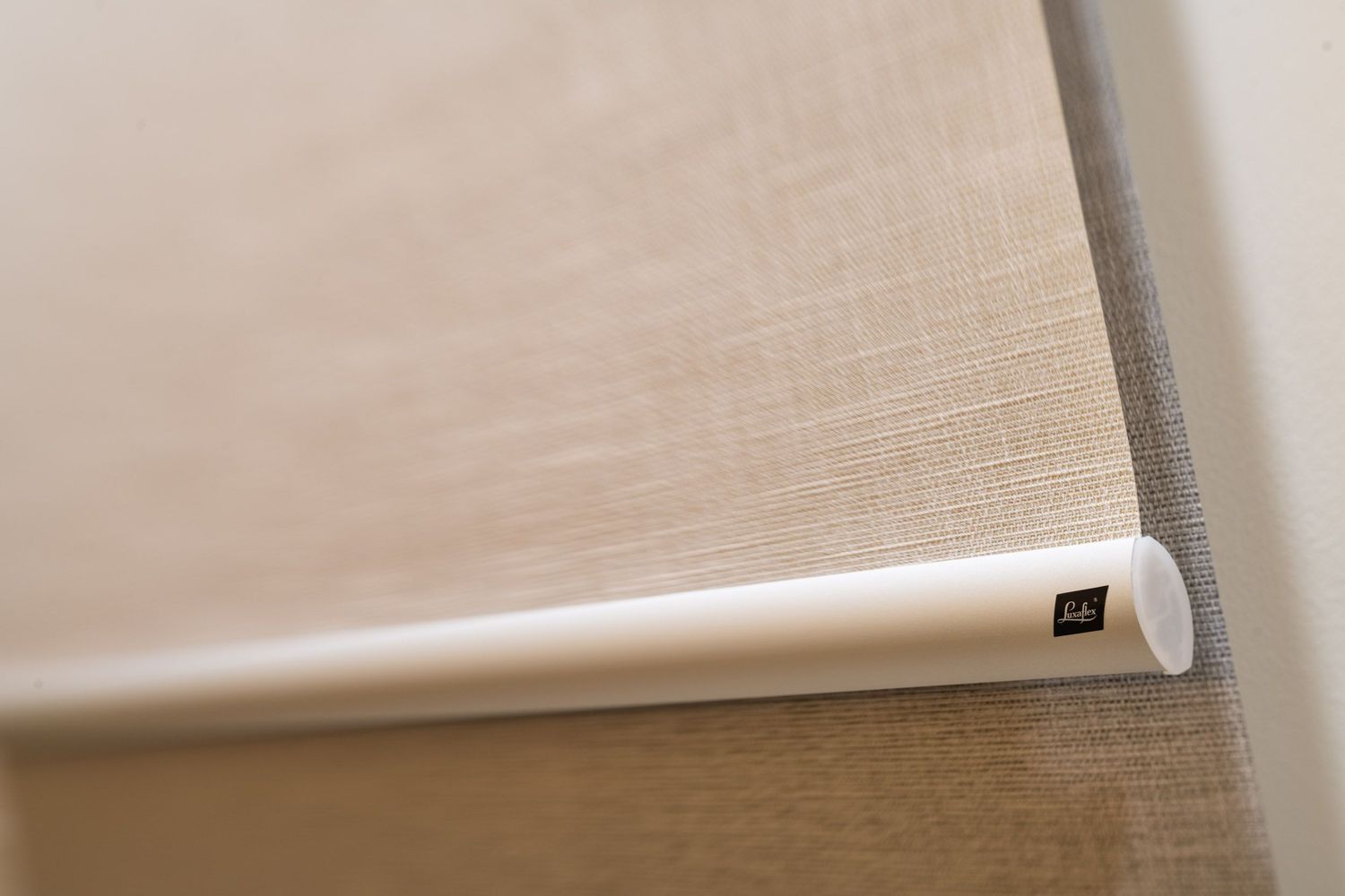 Close-up detail of a beige roller blind with white bottom bar and small brand label on a window.
