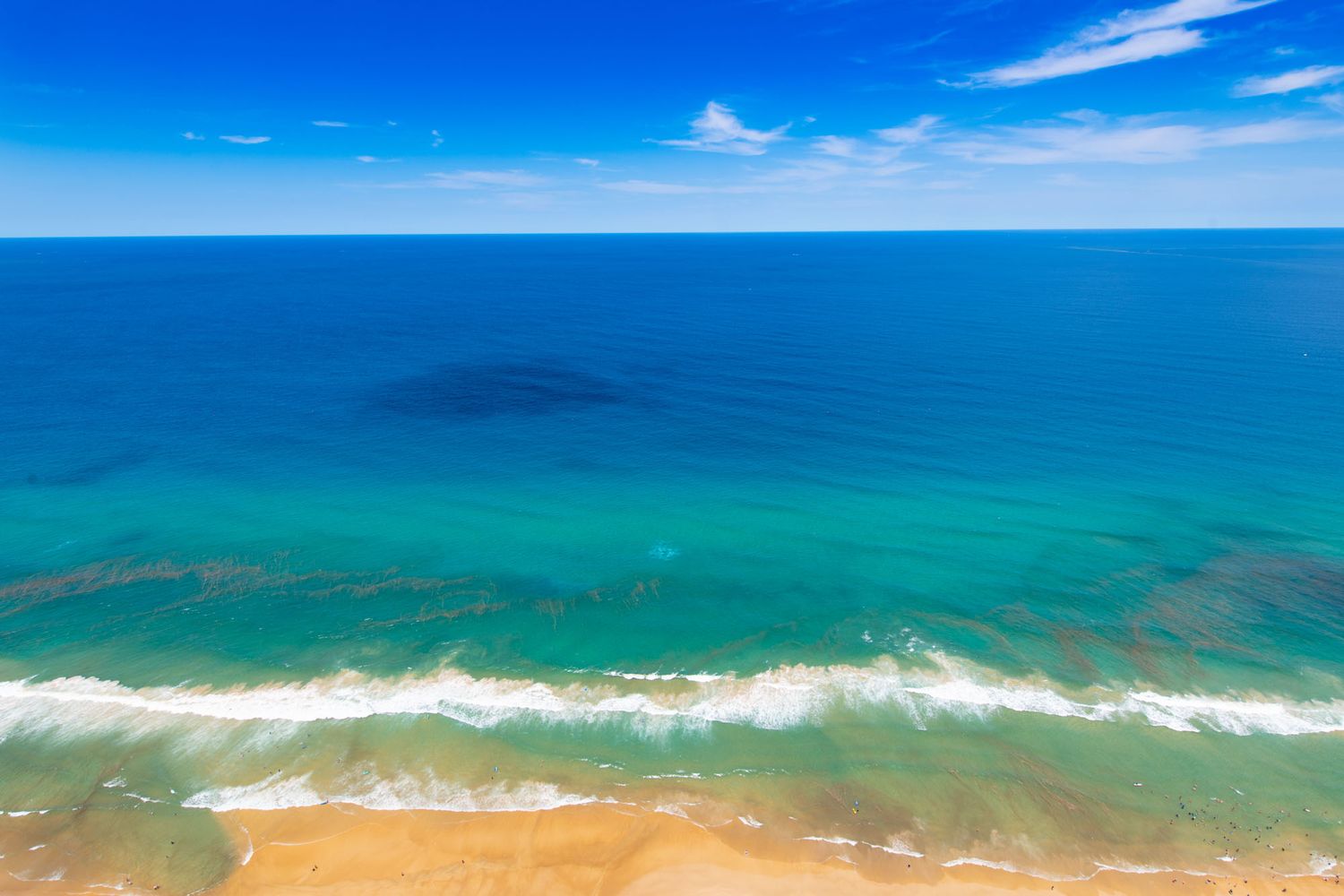 Aerial view of turquoise ocean waves meeting golden sandy beach under bright blue sky.