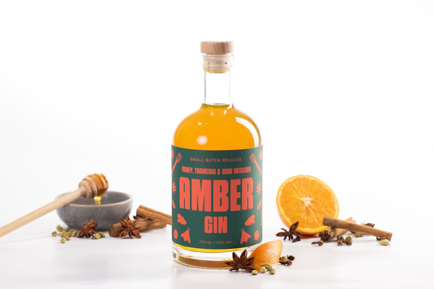 Bottle of Amber Gin with honey, cinnamon, star anise, and fresh orange slices on white background.