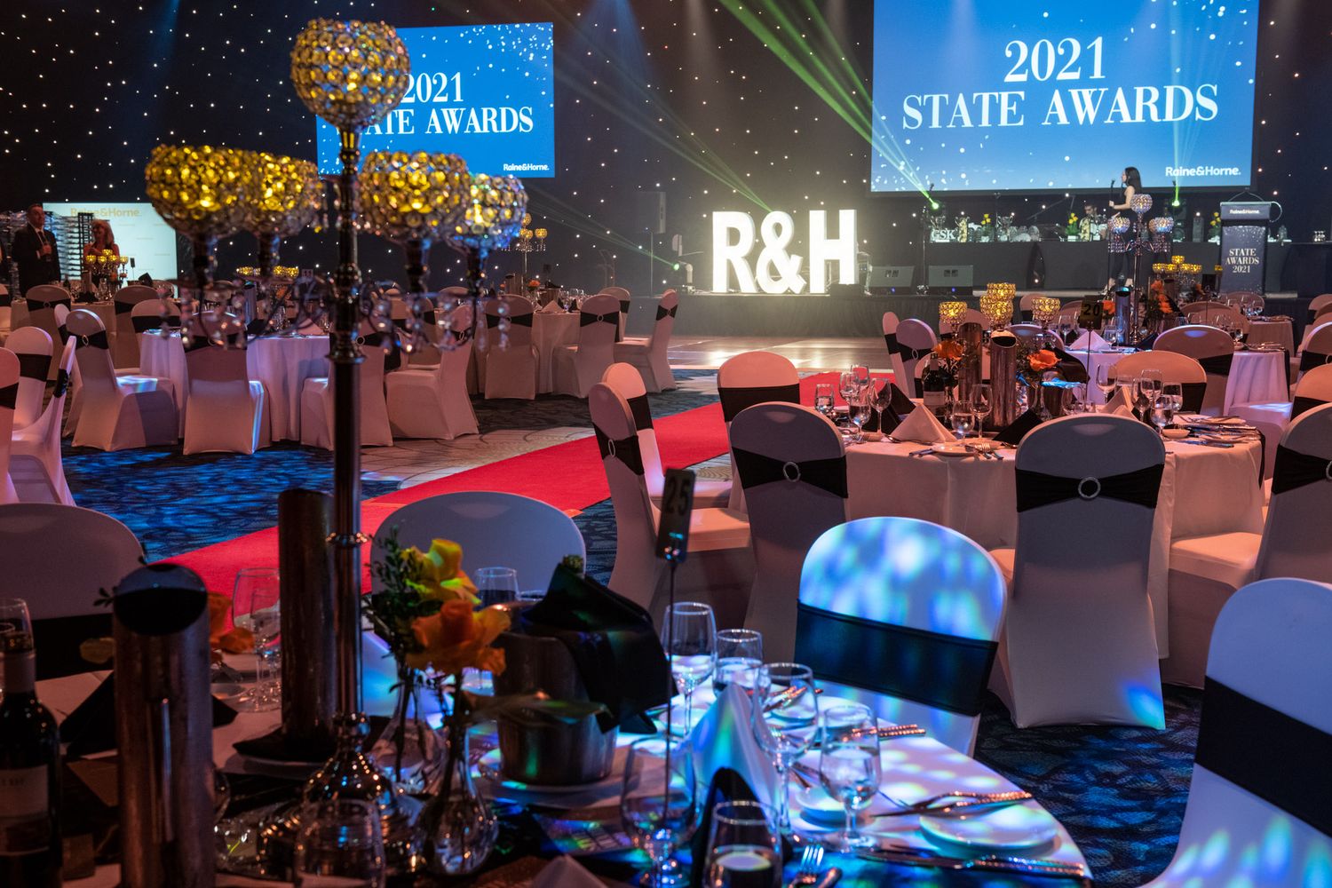 Elegant 2021 State Awards gala dinner with R&H monogram letters, blue lighting, and formally set round tables.