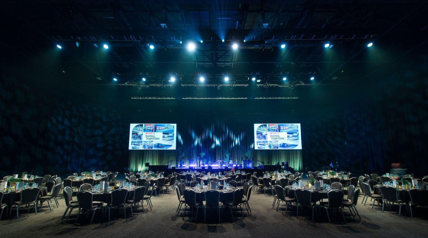 Elegant large-scale gala dinner setup with round tables and dual projection screens.