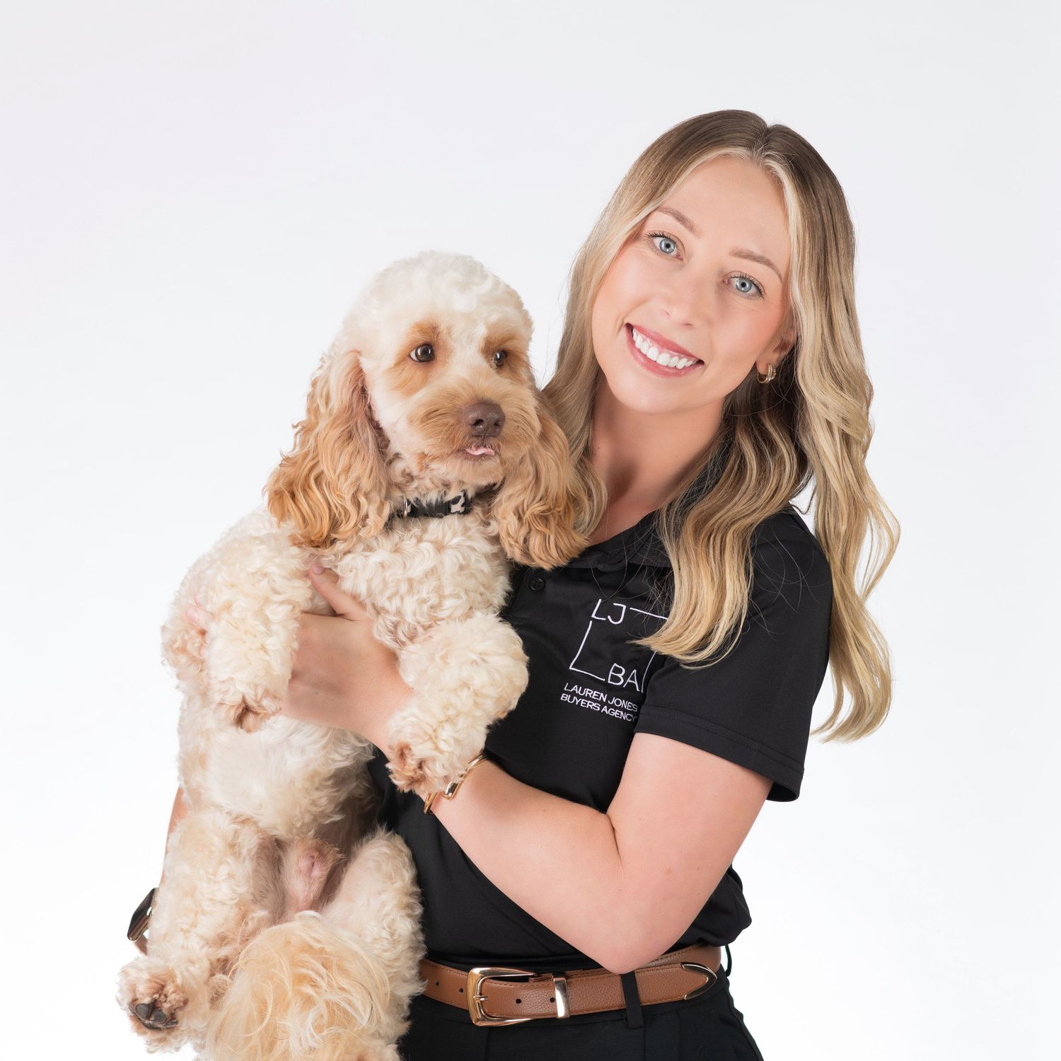 Smiling blonde woman in black polo shirt holding a fluffy cocker spaniel dog, professional portrait.
