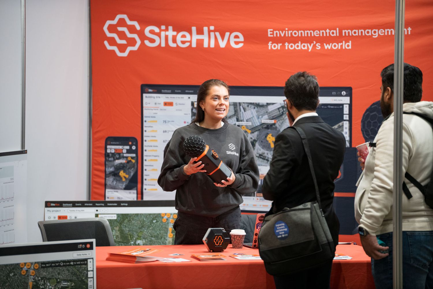 Woman presenting SiteHive environmental management software at a red branded exhibition booth.