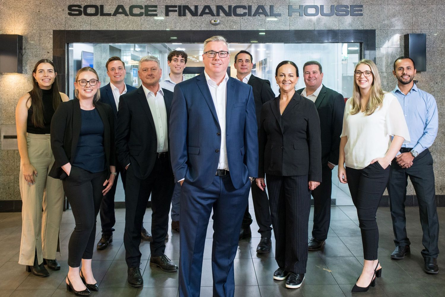 Professional corporate team posing in modern office lobby of Solace Financial House building.