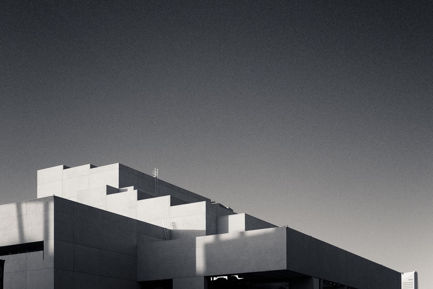 Minimalist brutalist architecture building with geometric stepped roofline against a gray sky in black and white.
