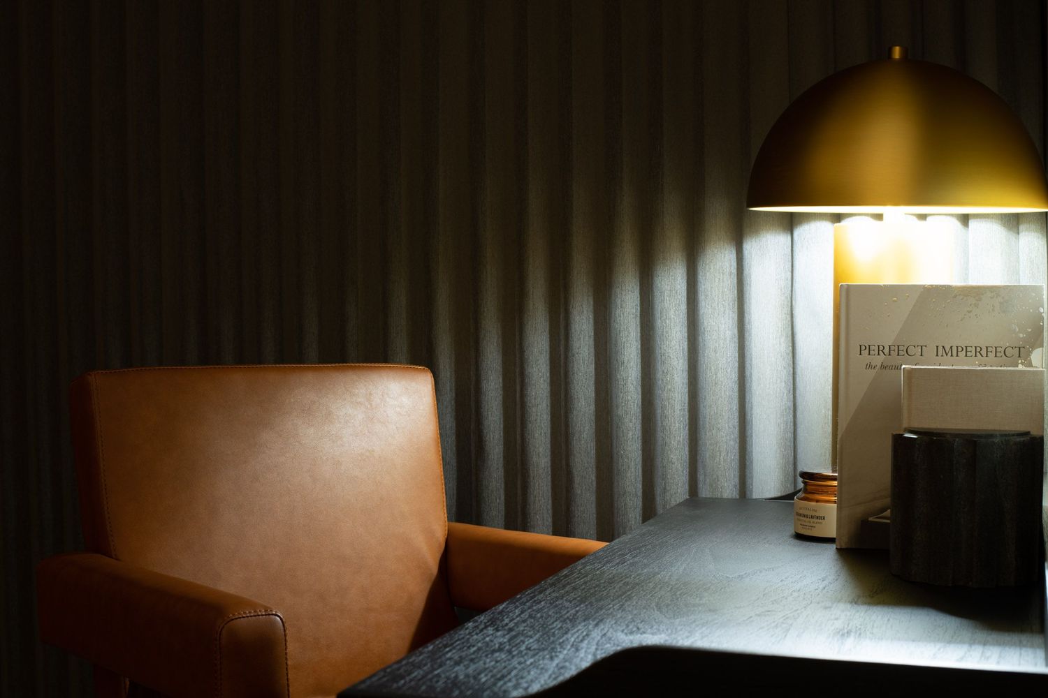 Leather armchair beside illuminated gold pendant lamp in dark moody interior.