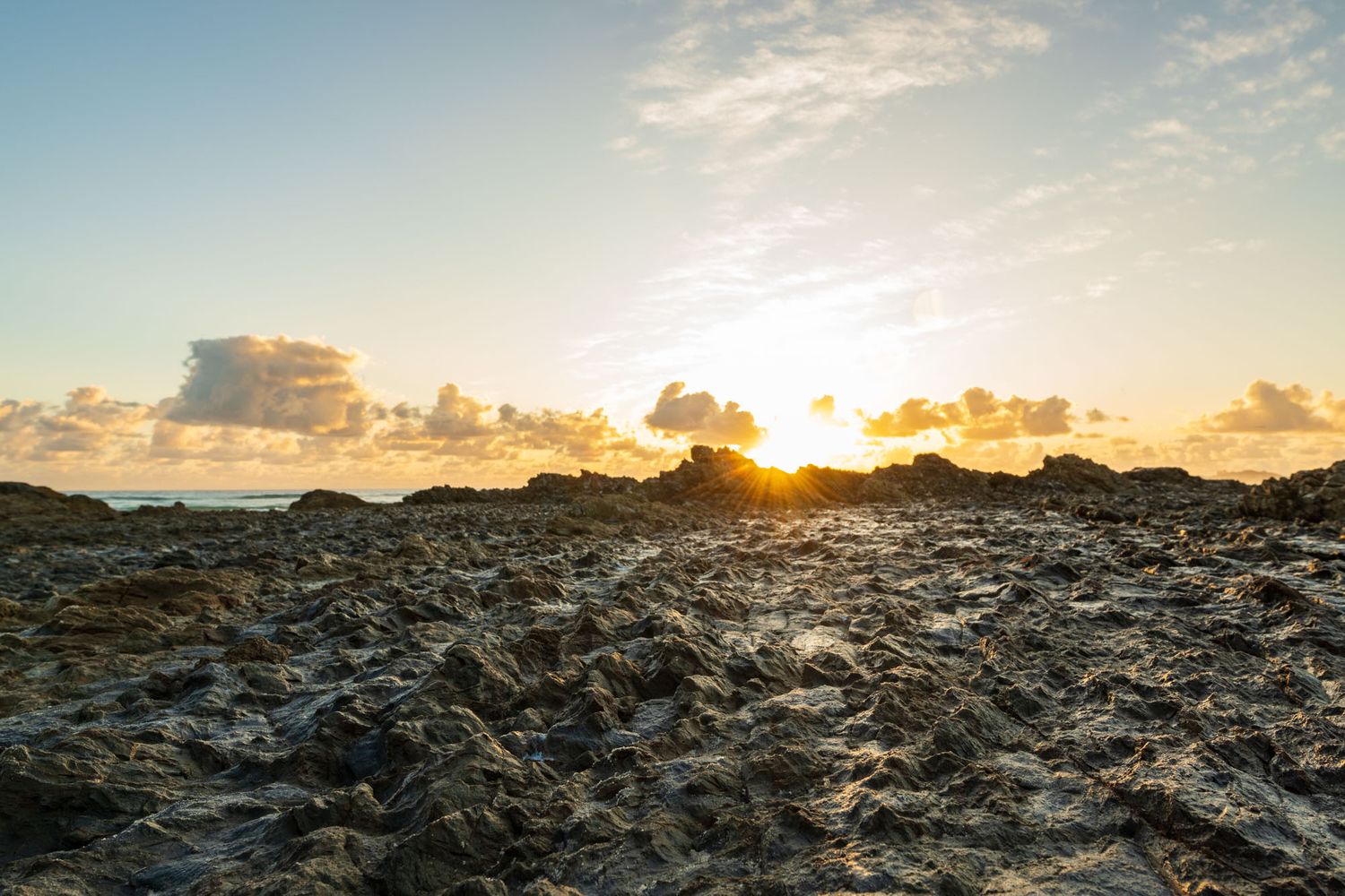 Rugged rocky landscape at sunset with golden sun rays breaking through clouds over the horizon.
