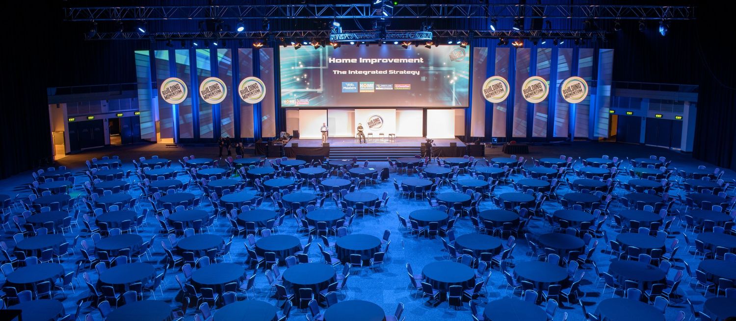 Large conference hall with round tables and a lit stage for a corporate awards ceremony.