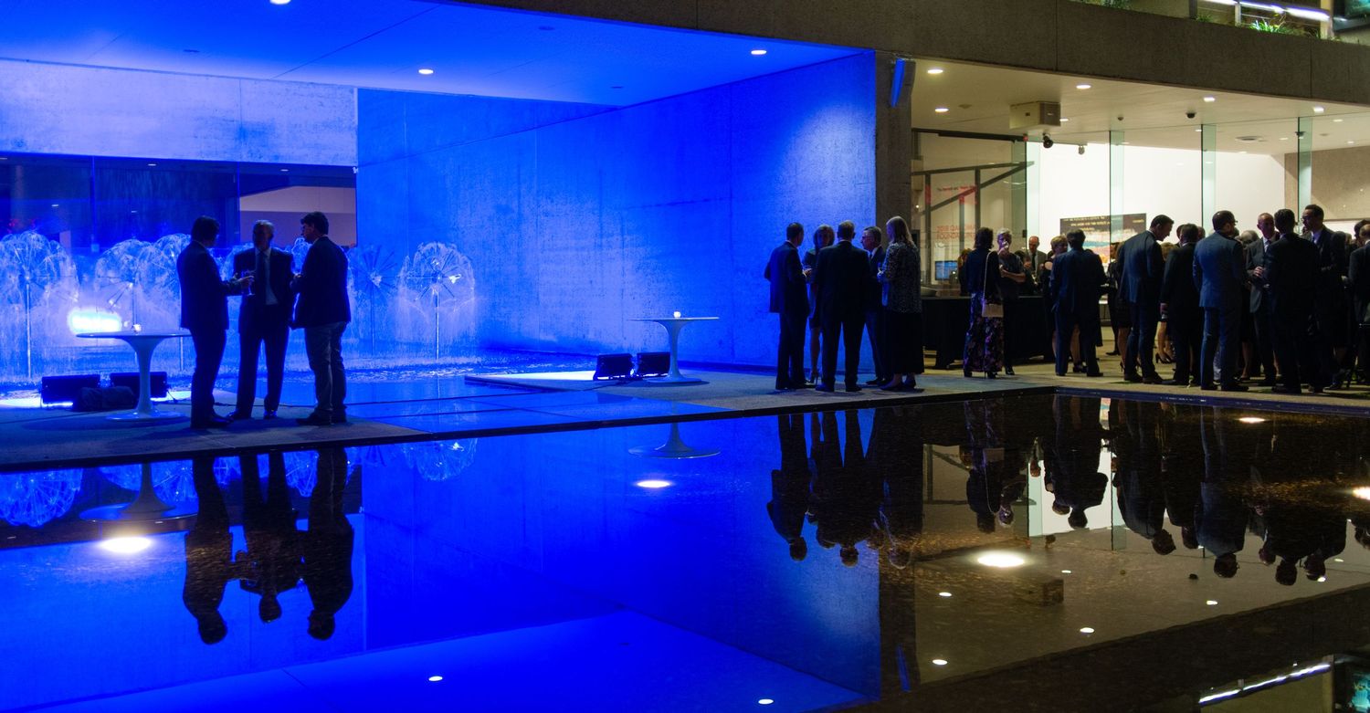 Elegantly dressed guests networking beside a reflective pool illuminated by blue lighting at a corporate event.