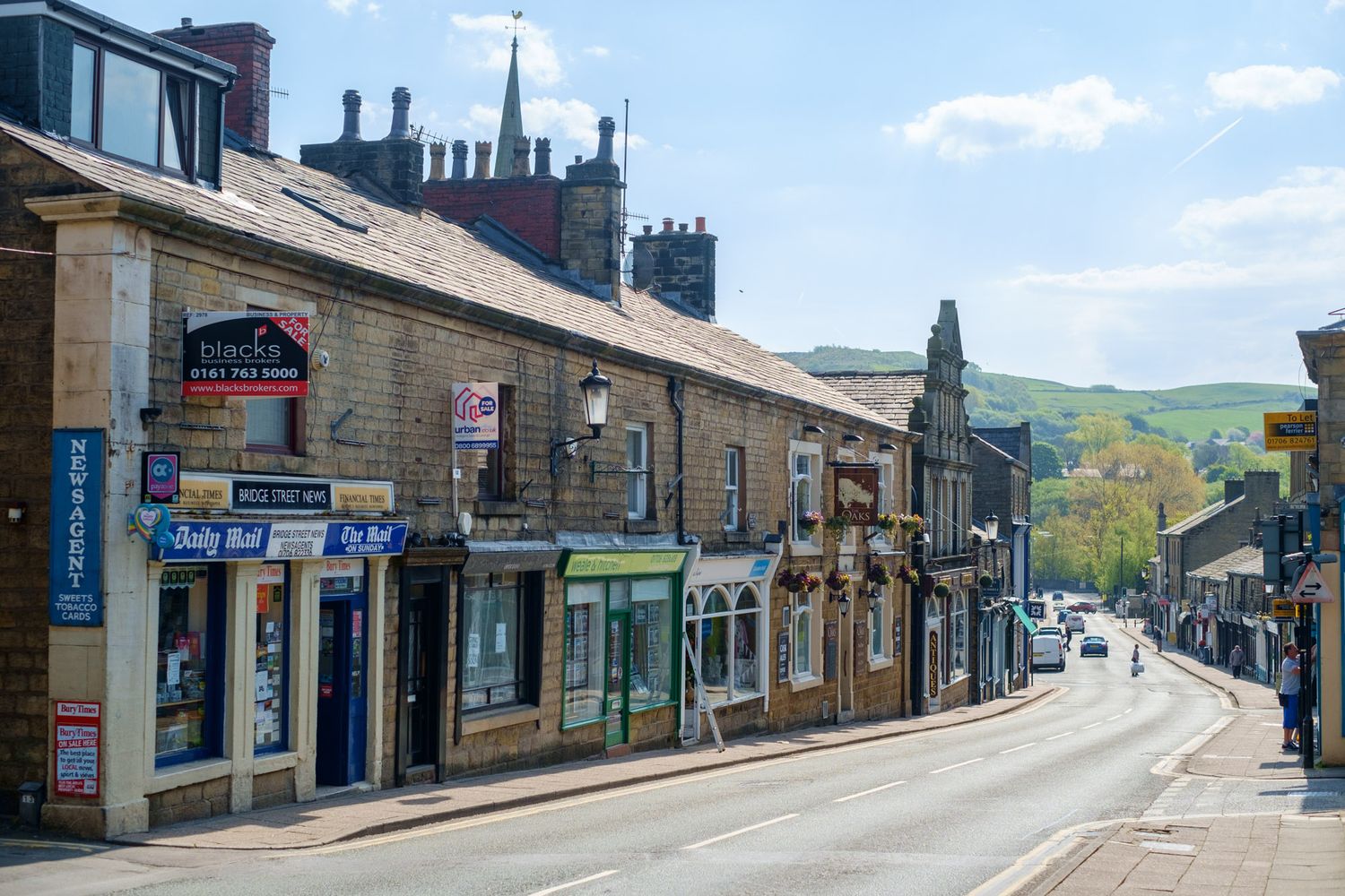 Charming English market town high street with stone buildings, shops and church tower in background.