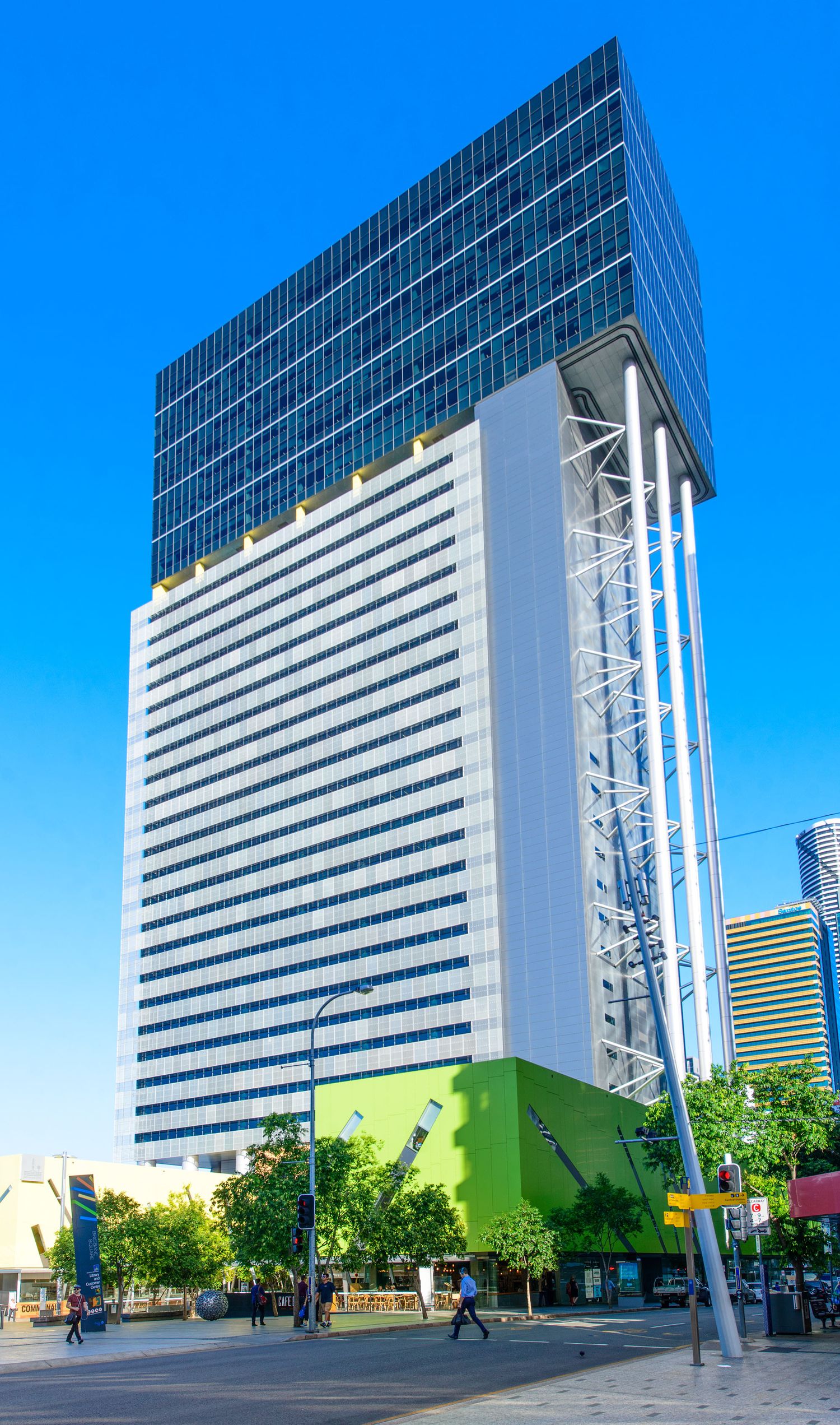Tall modern glass office tower with green base and scaffolding under blue sky in city.