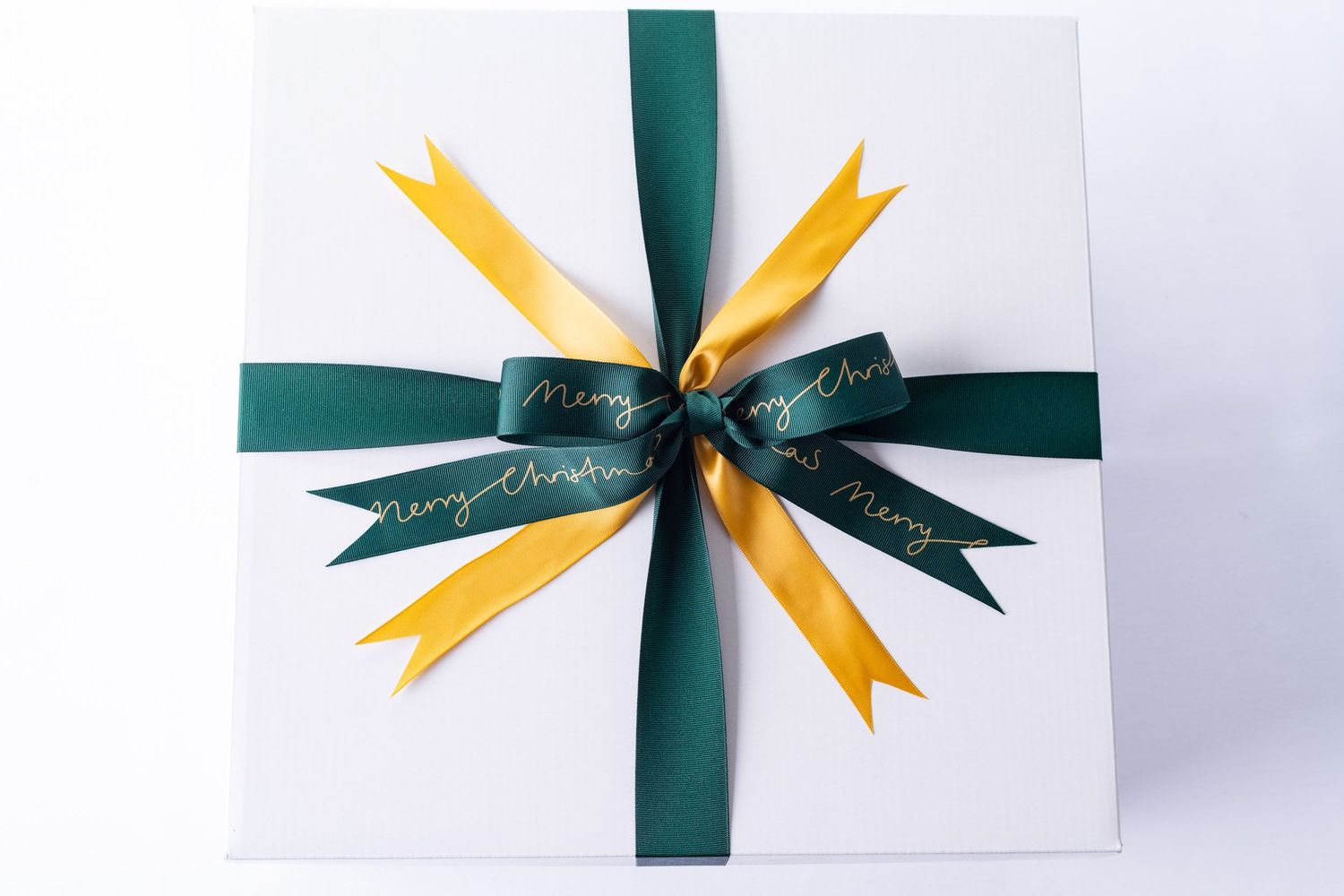 White Christmas gift box with green and gold Merry Christmas ribbon bow on white background.