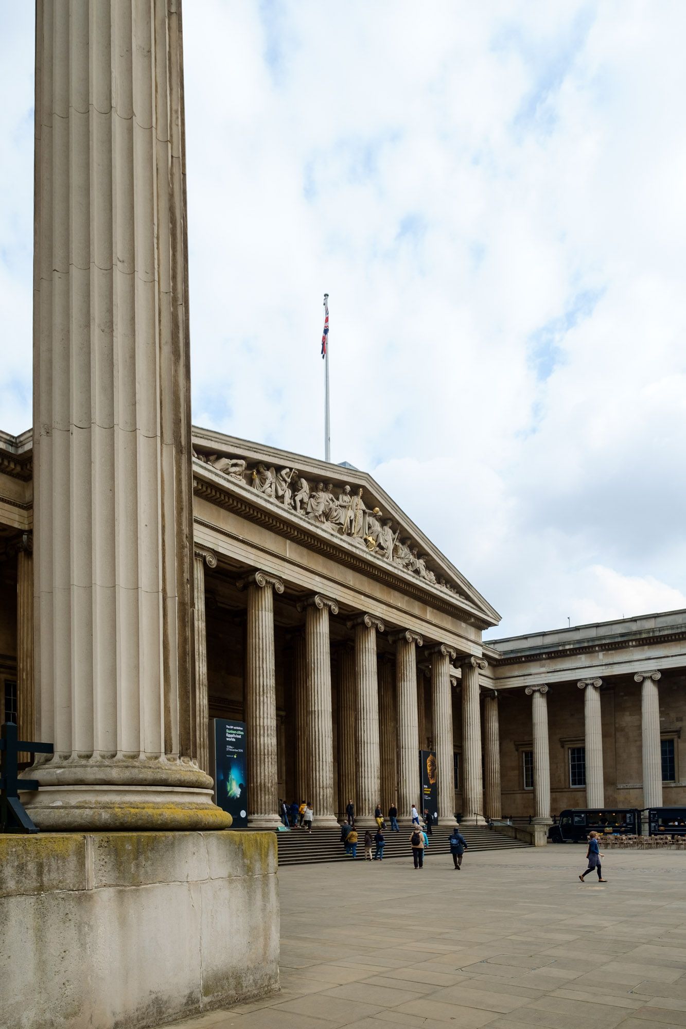 The British Museum's iconic Greek Revival facade with tall columns and visitors walking outside in London.