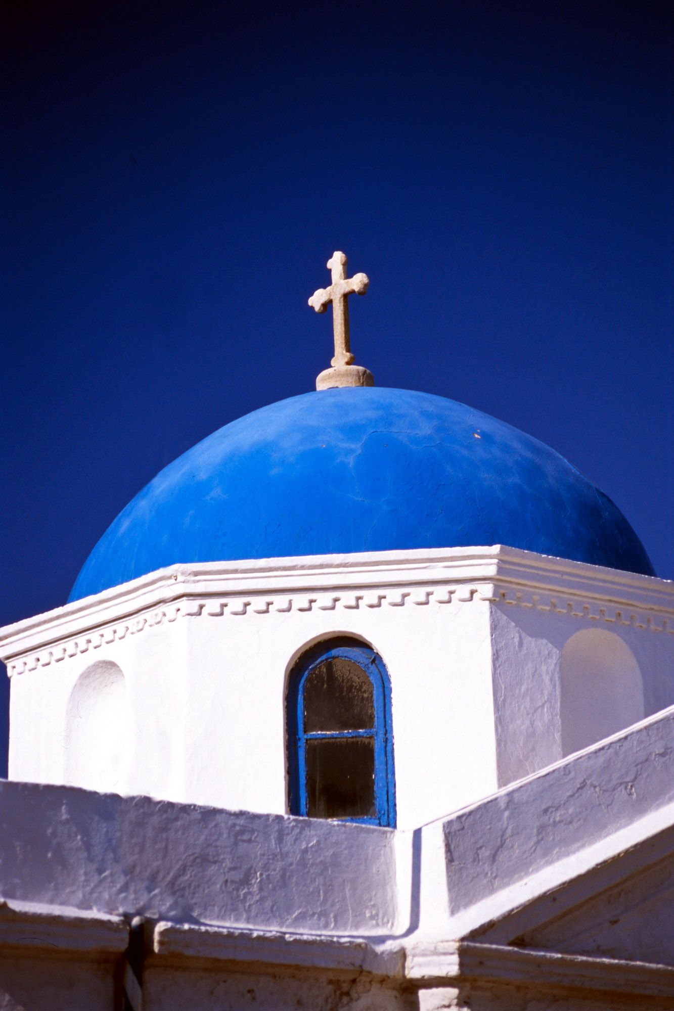 Iconic white Greek Orthodox church with vivid blue dome and golden cross against deep blue sky.