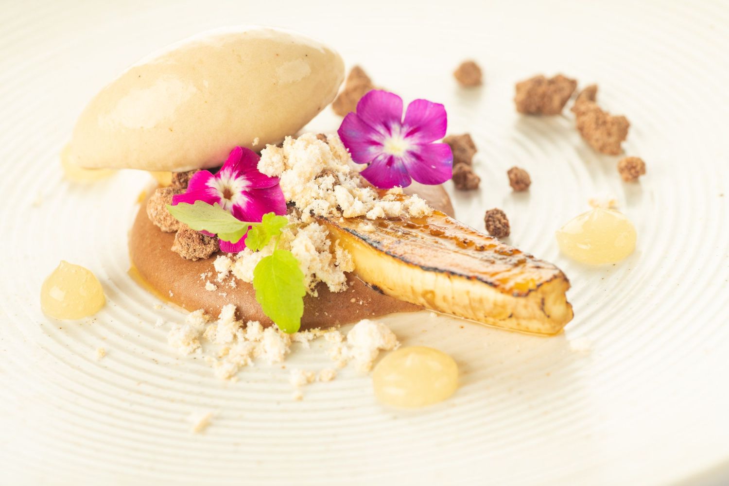 Gourmet dessert plate with caramelized tart, ice cream, edible flowers, and crumble.