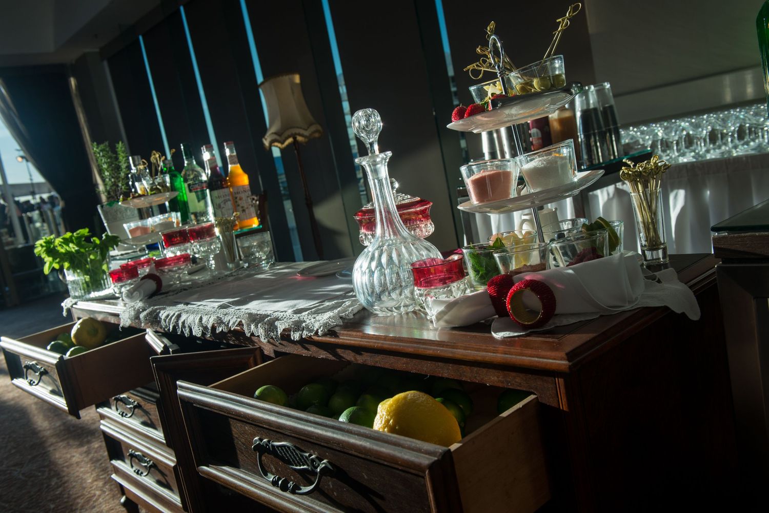 Elegant bar setup with crystal glassware, decanters, and fresh garnishes on a wooden sideboard.