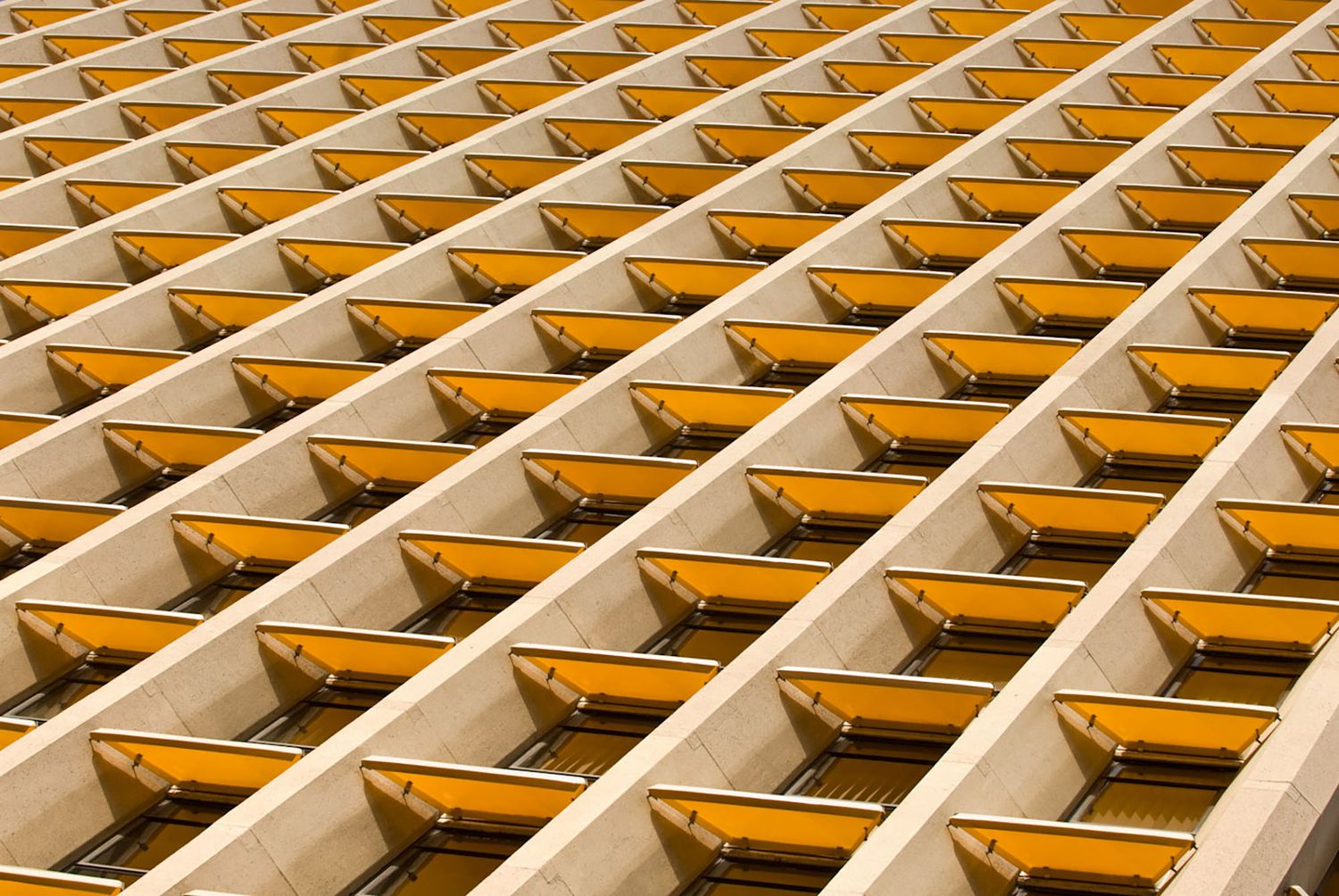 Abstract architectural pattern of repetitive yellow and beige geometric building facade with diagonal lines.