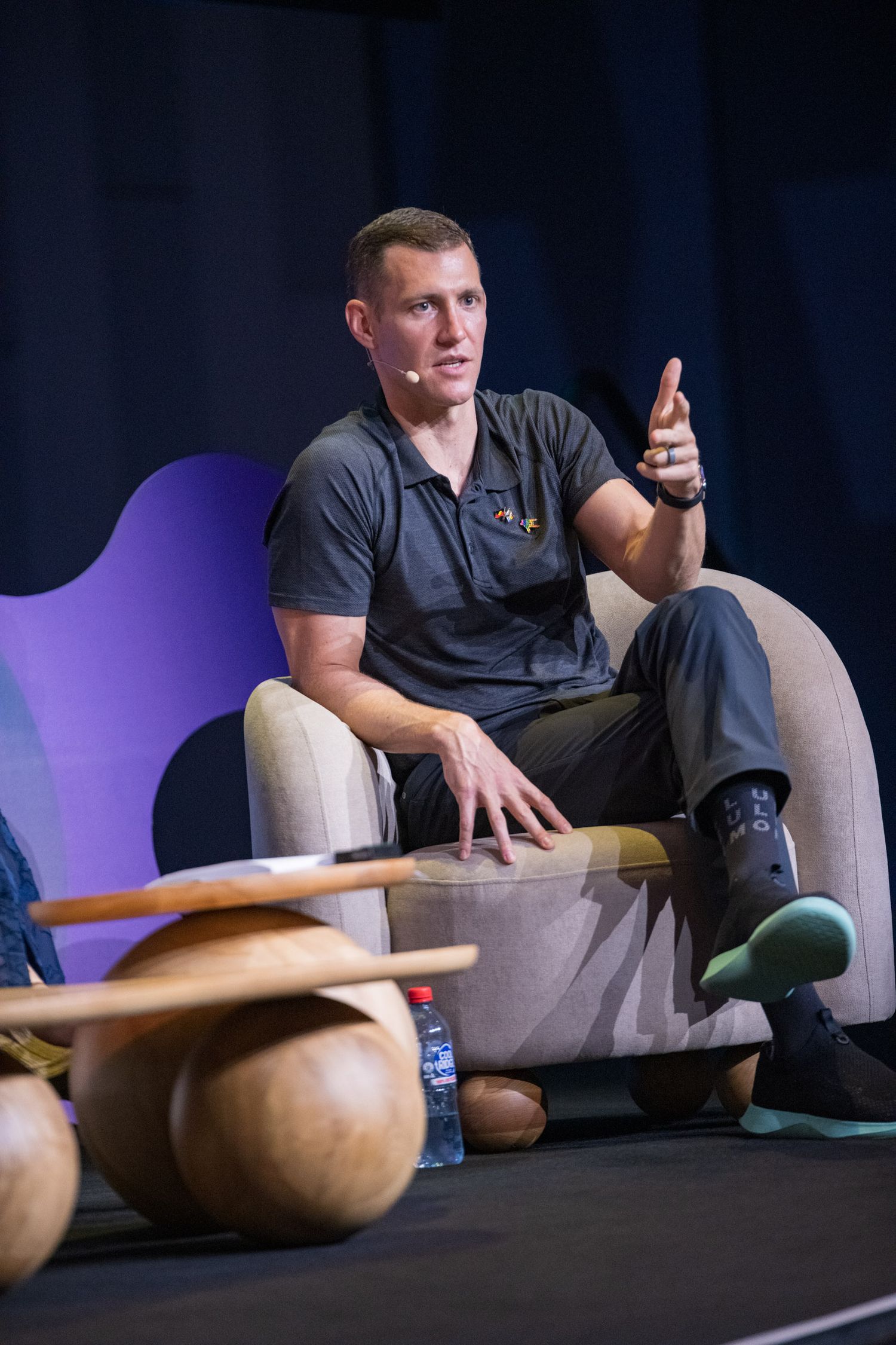 Young man in dark polo shirt speaks gesturing with finger during conference panel discussion.