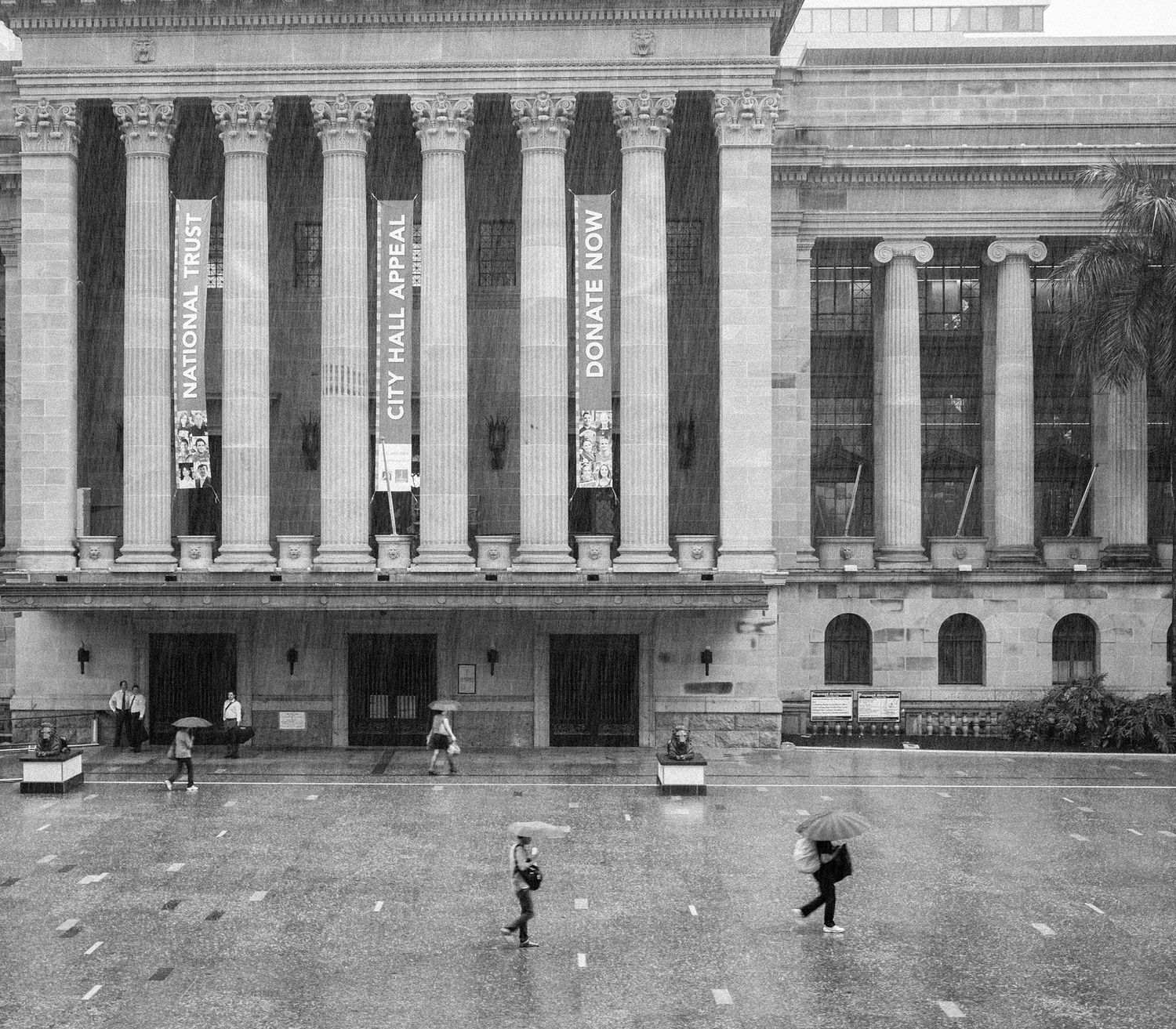 Black and white photo of a grand neoclassical building with tall columns and banners in the rain.