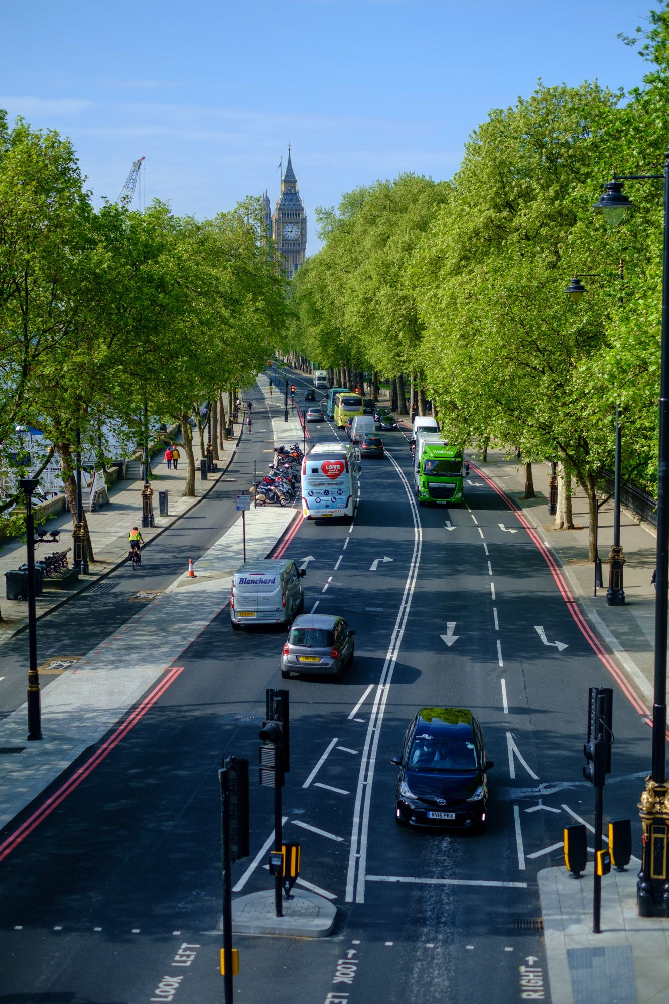 Tree-lined London street with traffic leading toward Big Ben on a sunny day.