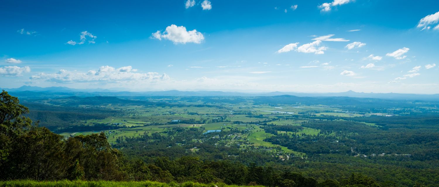 Panoramic aerial view of a vast lush green valley and farmland stretching to the horizon under a blue sky.