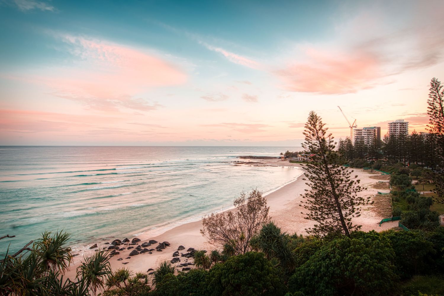 Stunning pink and orange sunset over a tropical beach with tall pine trees.