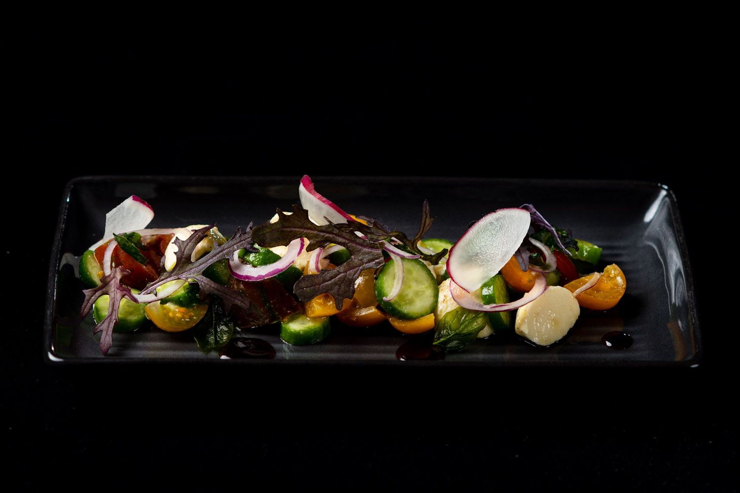 Fresh colorful vegetable salad with radishes, cucumber, and cherry tomatoes on a dark rectangular plate.