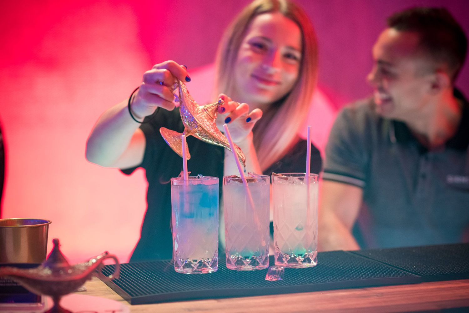 Bartender pouring drinks at colorful cocktail bar.