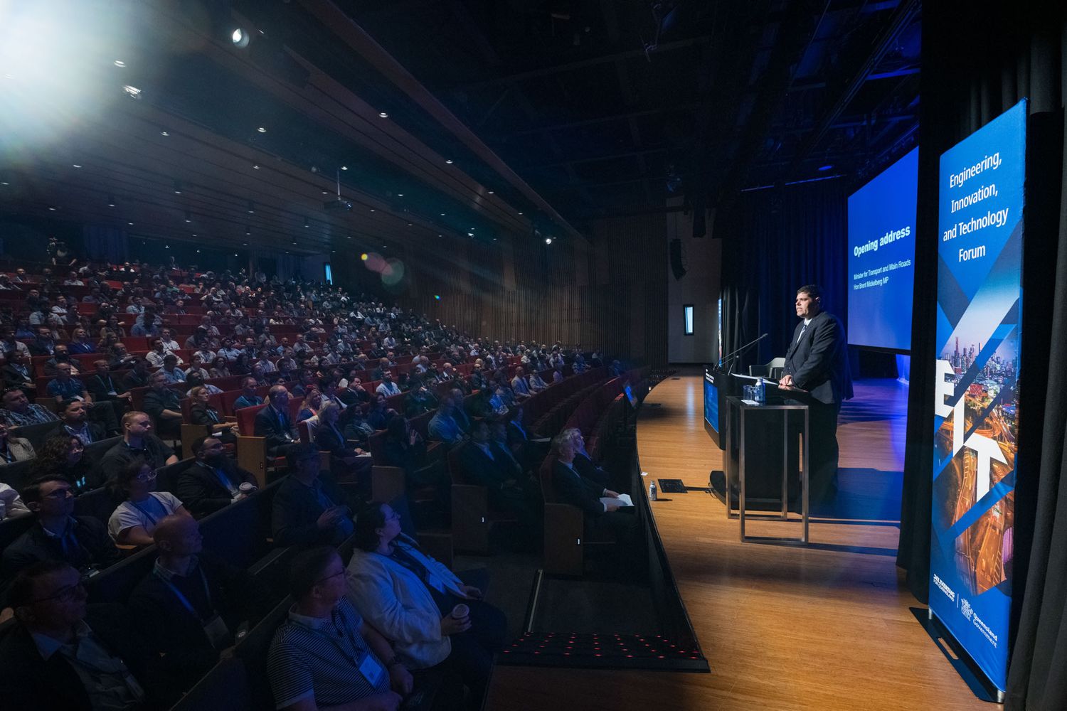 Speaker presenting to large audience in packed auditorium at engineering technology conference.