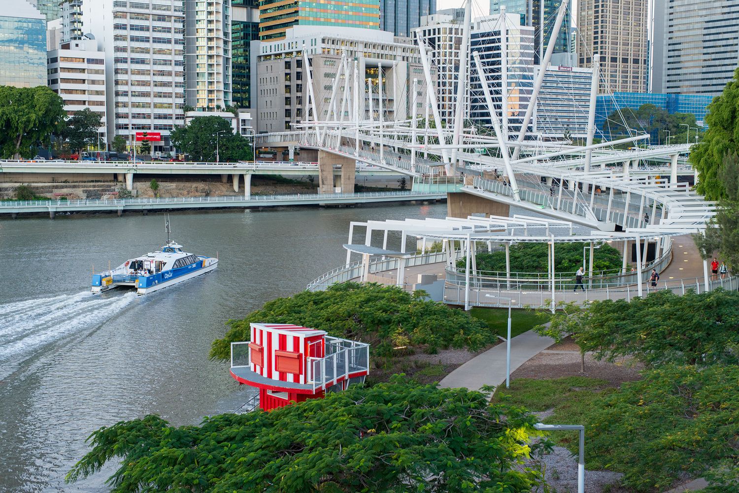 Aerial view of Brisbane River with a ferry, Kurilpa Bridge, and lush green parklands.
