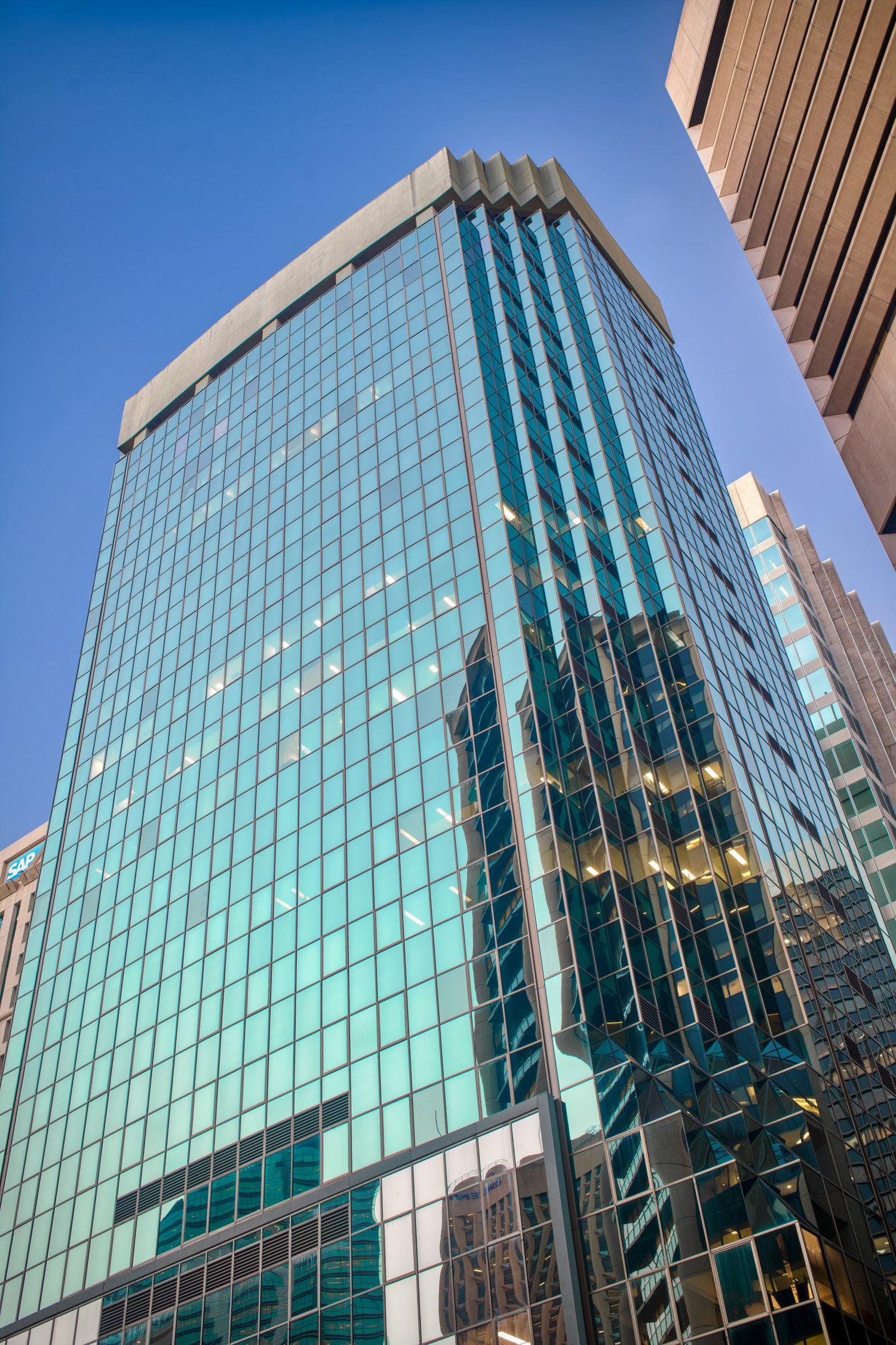 Modern glass office skyscraper reflecting surrounding buildings against a clear blue sky.
