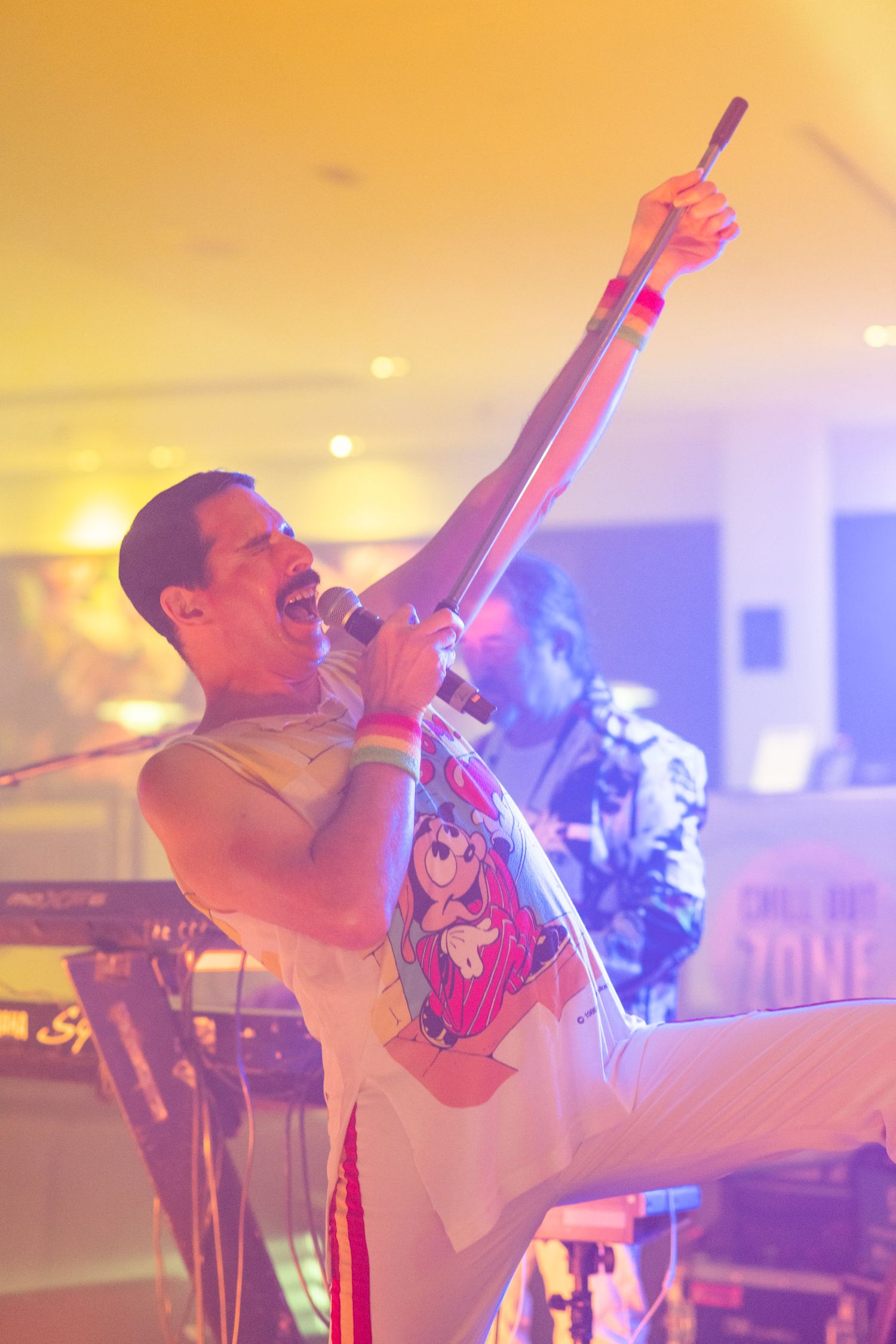 Energetic male singer performing live on stage under warm yellow spotlight with microphone raised.