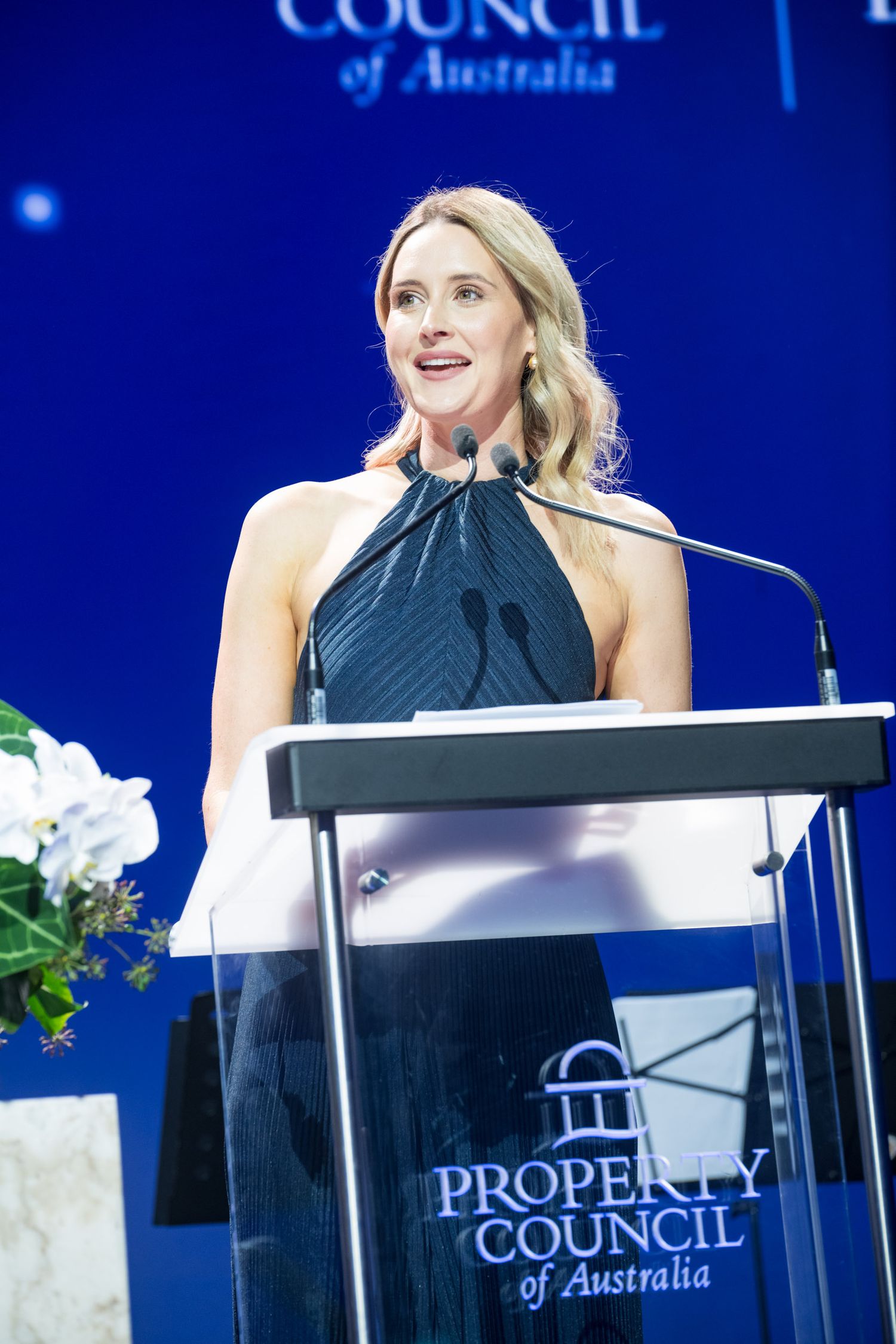 Blonde woman in black halterneck dress speaking at a Property Council of Australia podium on stage.