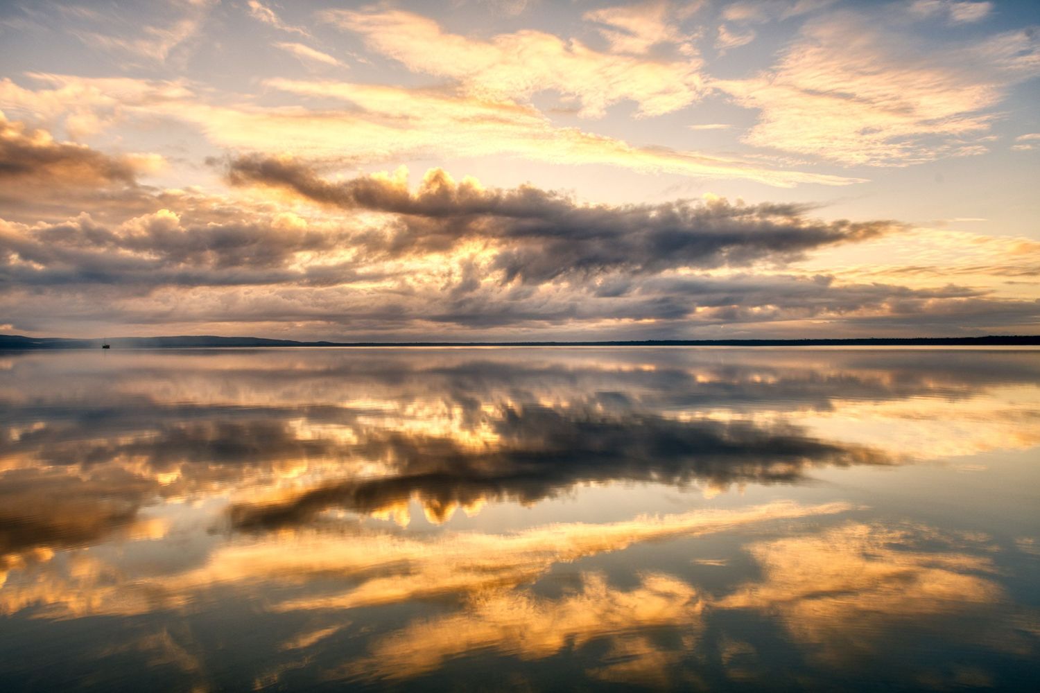 Dramatic golden sunset clouds perfectly reflected on the mirror-like surface of a tranquil lake.