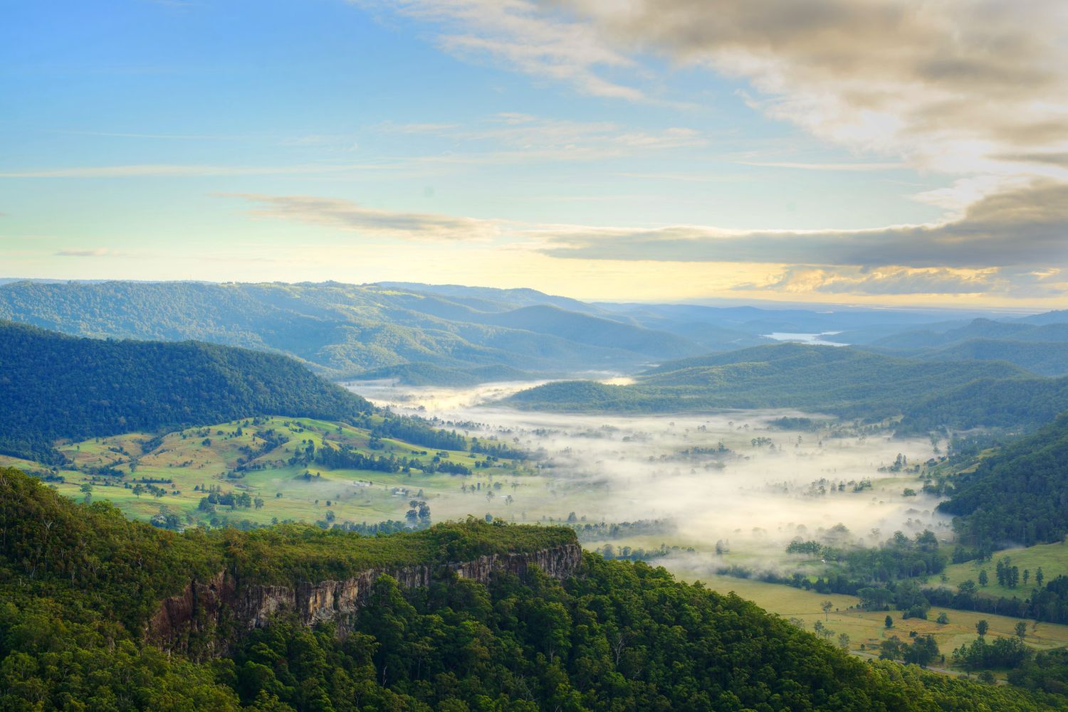 Aerial view of misty green valley with fog rolling through mountains at sunrise in Australia.